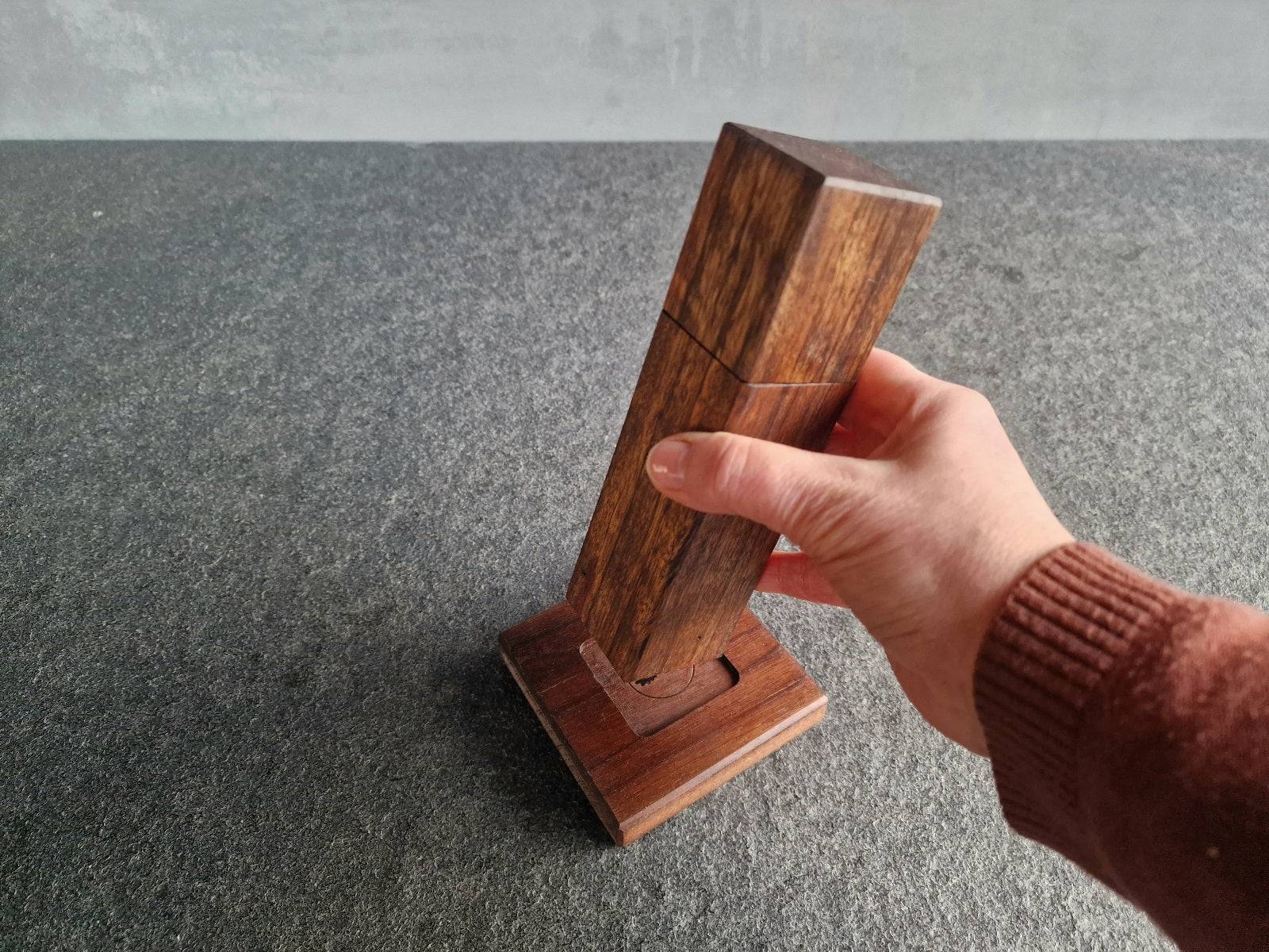 Hand hält eine Pfeffermühle aus Ovenkol über einem Untersetzer aus Nussbaum.