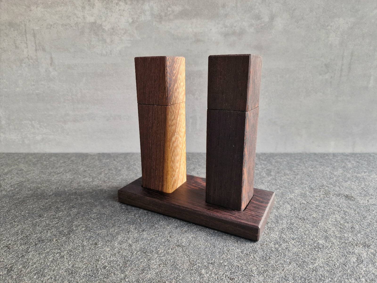 Wenge Salzmühle und Wenge Pfeffermühle auf einem Untersetzer. Die Mühlen haben ein Strässler Mahlwerk.