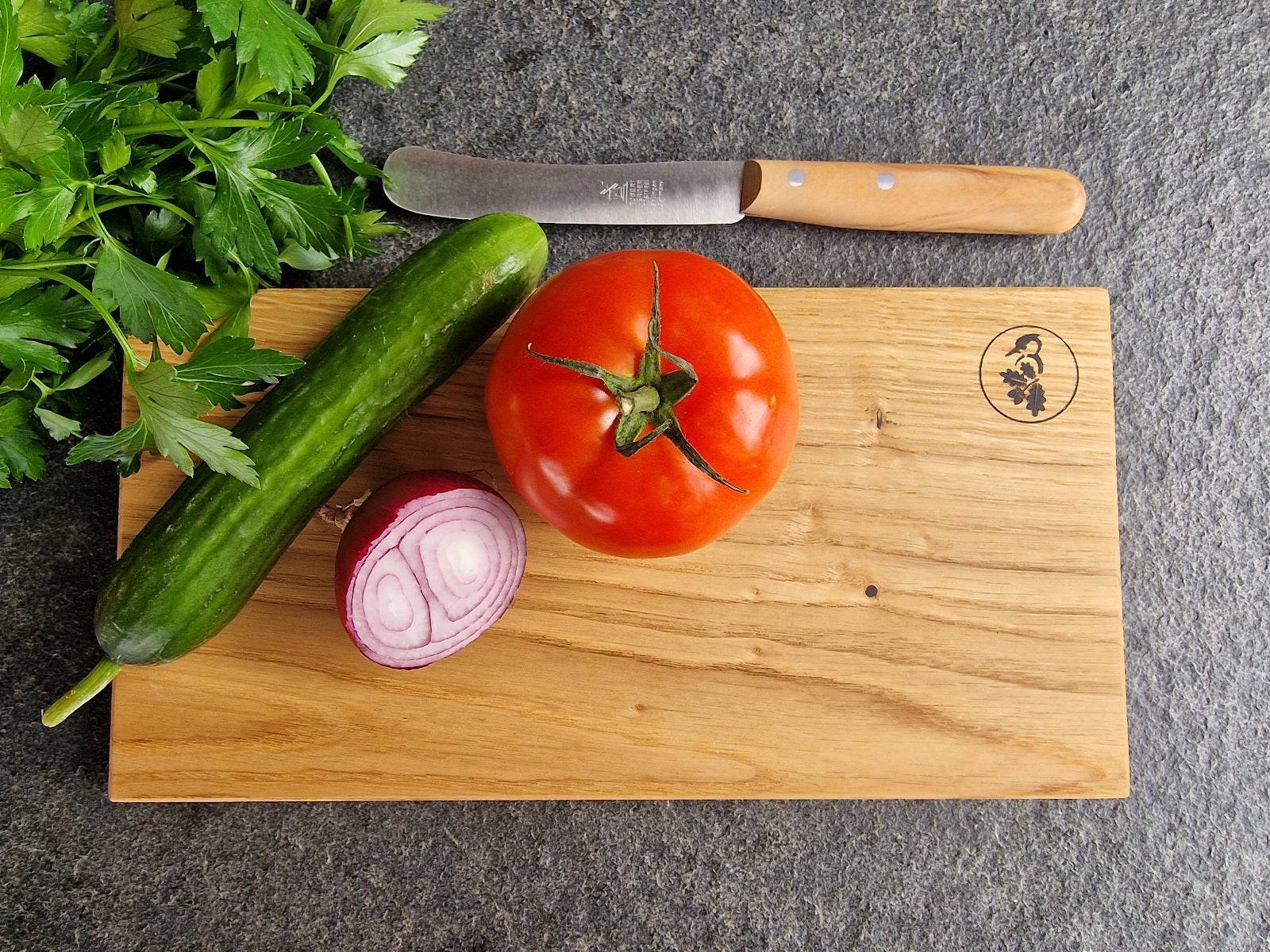 Brotzeitbrett mit Gurke und Tomate, Zwiebel und einem Brotzeitmesser Buckels mit Olive-Griff.