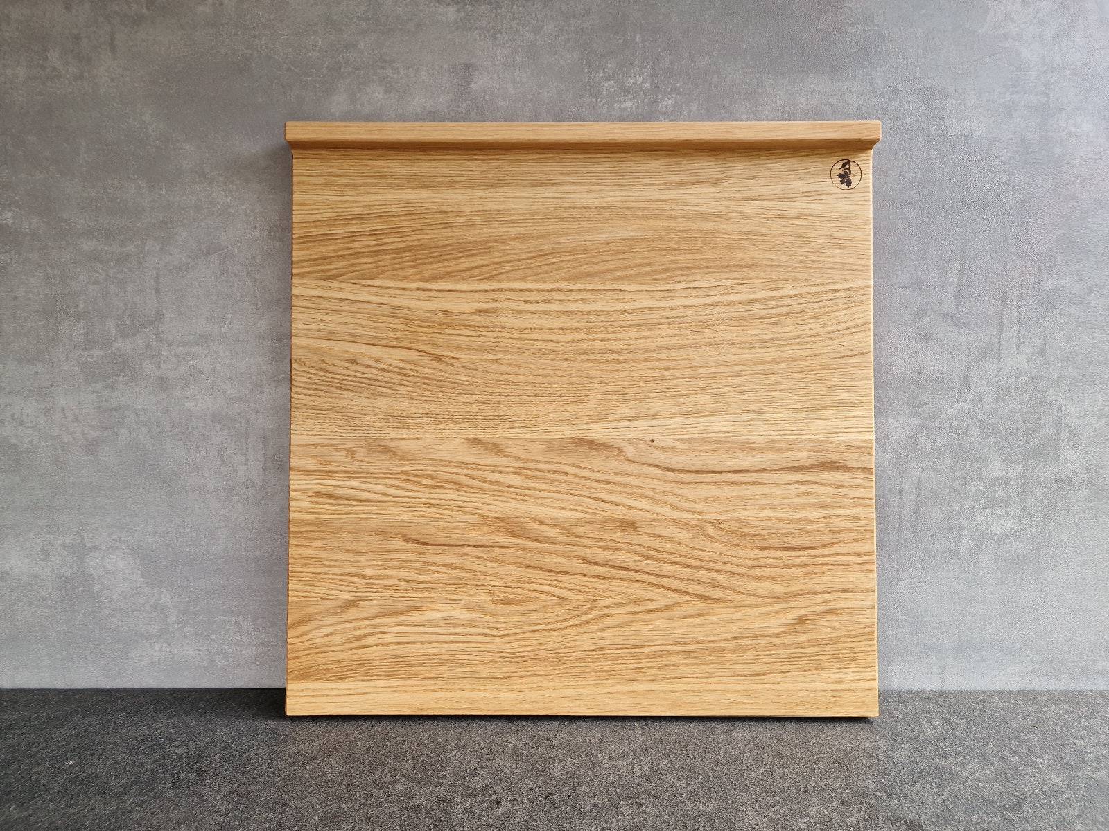 Quadratisches leichtes Backbrett aus 3-Schicht-Eiche mit 2 Anschlägen an einer Betonwand.