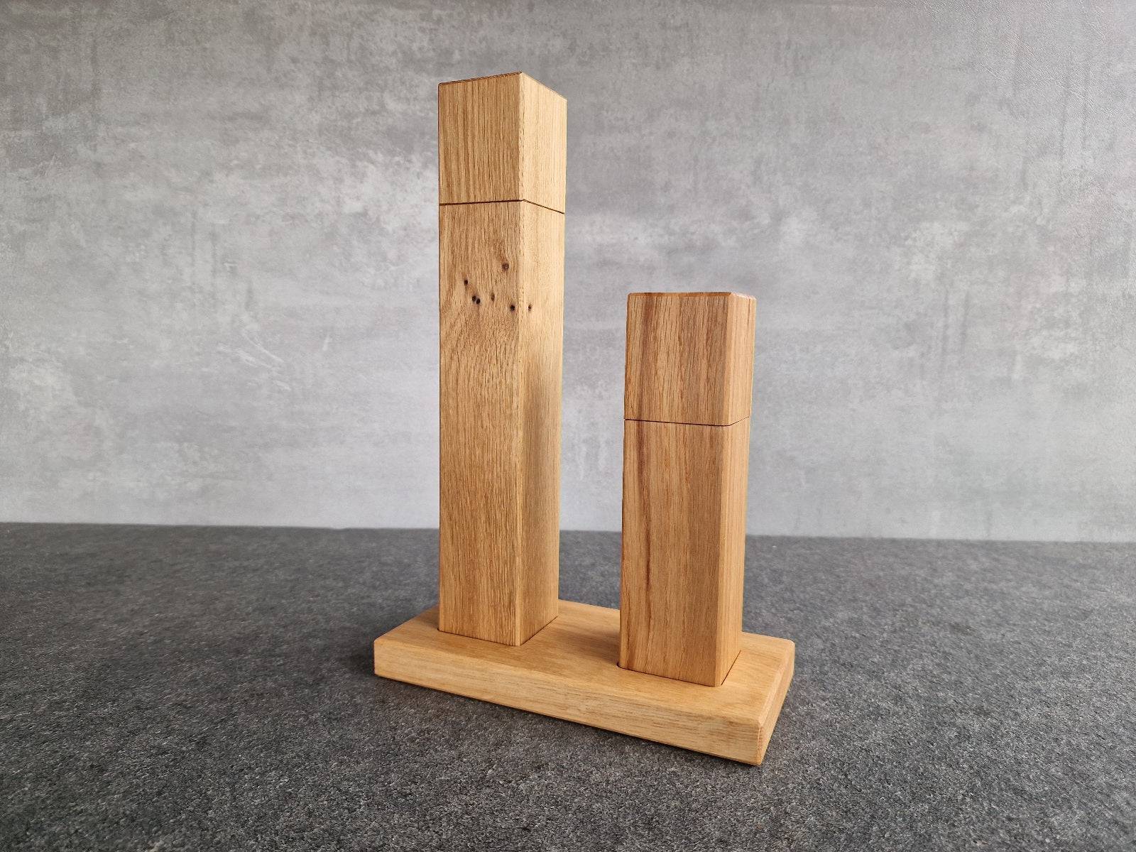 Vorne im Bild die kleine Pfeffermühle, dahinter die größere Salzmühle, beides aus Eiche. Die Mühlen stehen auf einem Untersetzer aus Eiche mit Mulden.