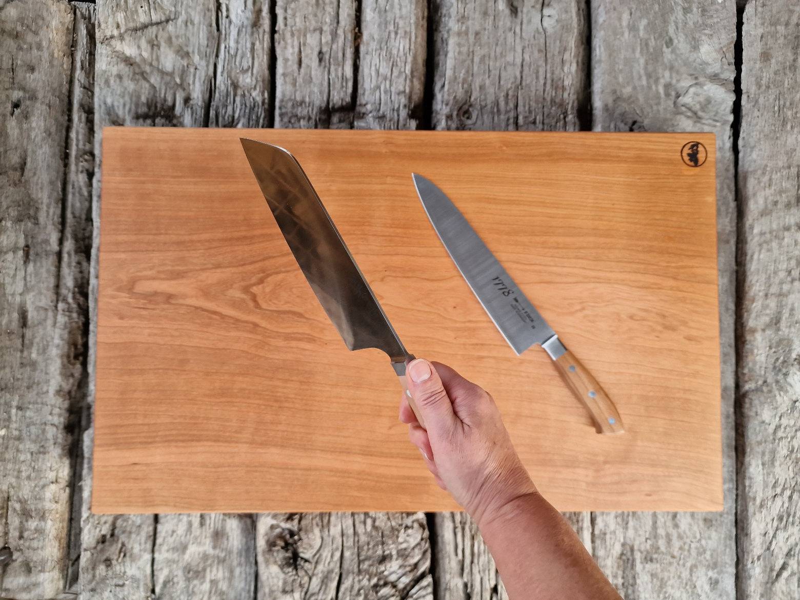 Hand hält ein Güde Kochmesser über einem Schneideblock aus Kirschbaum