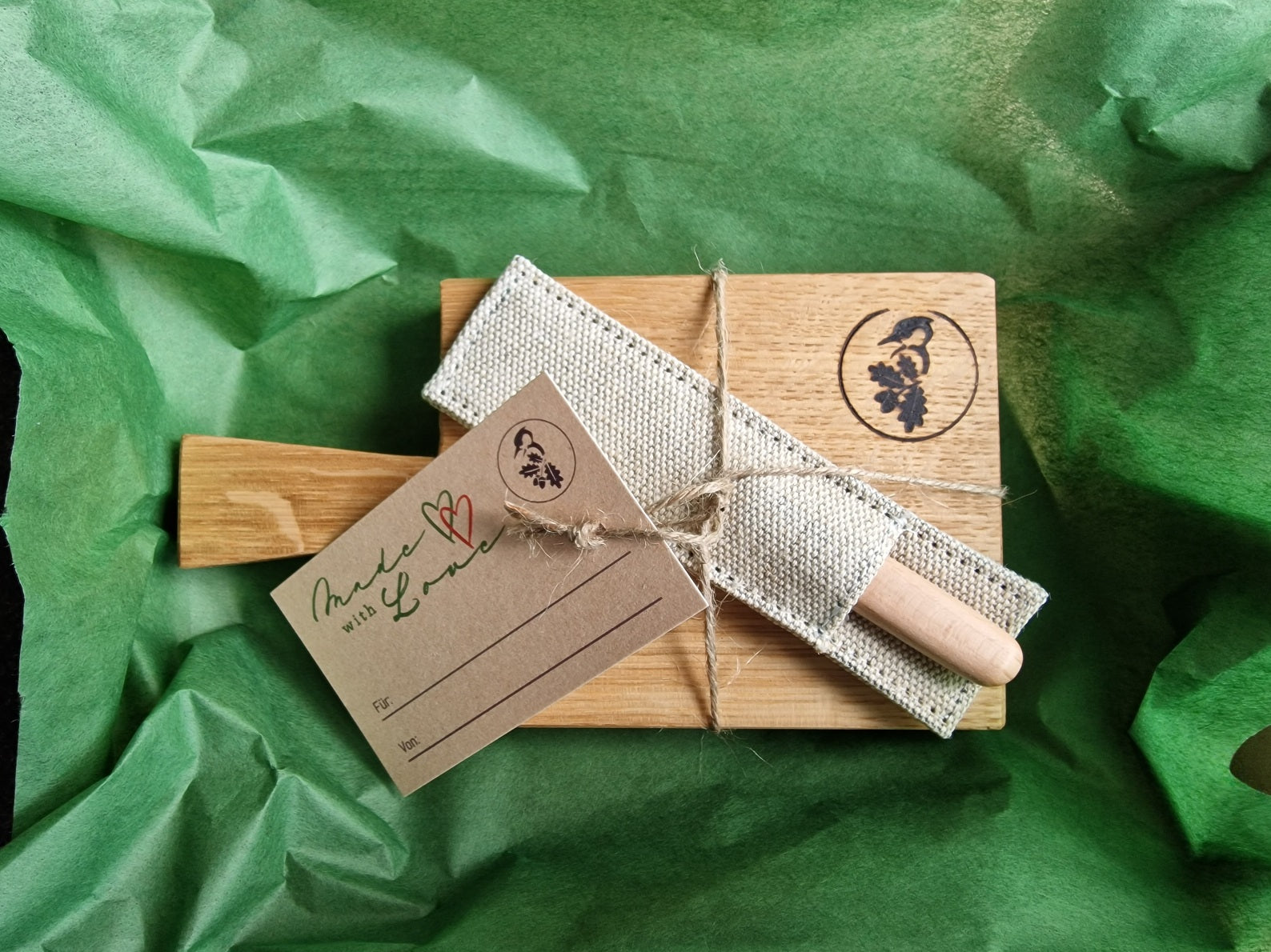 Amuse Gueule Brettchen mit Stiel und einem Buttermesser von Windmühlenmesser in einem grünen Seidenpapier gehüllt.