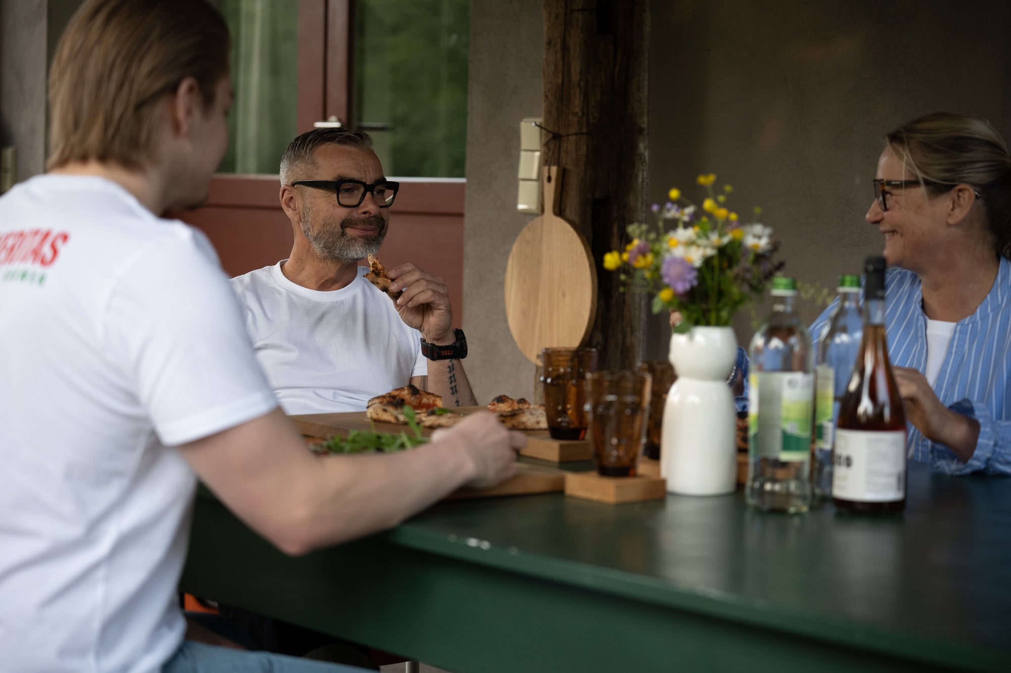 Eine lächelnde Familie sitzt auf der Terrasse am Tisch und isst Pizza.