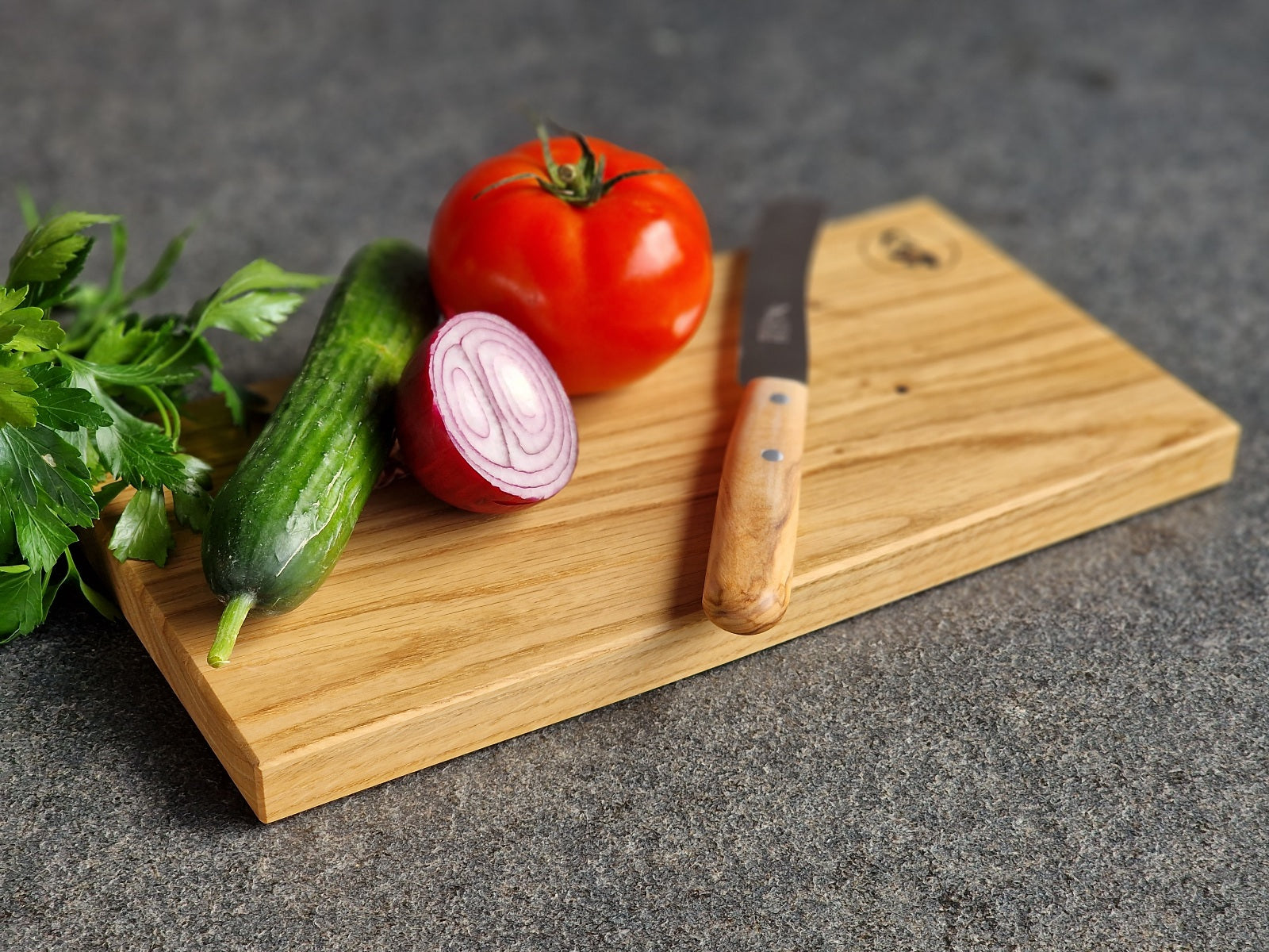 Brotzeitbrett mit Gurke und Tomate, Zwiebel und einem Brotzeitmesser Buckels mit Olive-Griff.