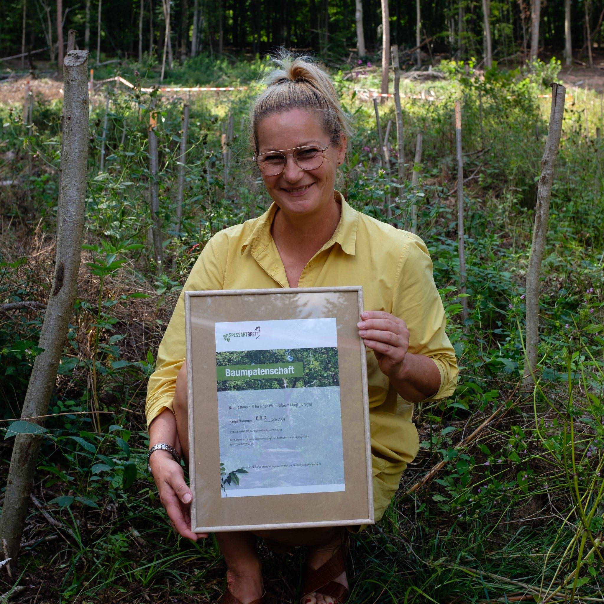 Eingerahmte Spessartbrett Urkunde über eine Baumpatenschaft im Spessart. Gezeigt von einer Frau.