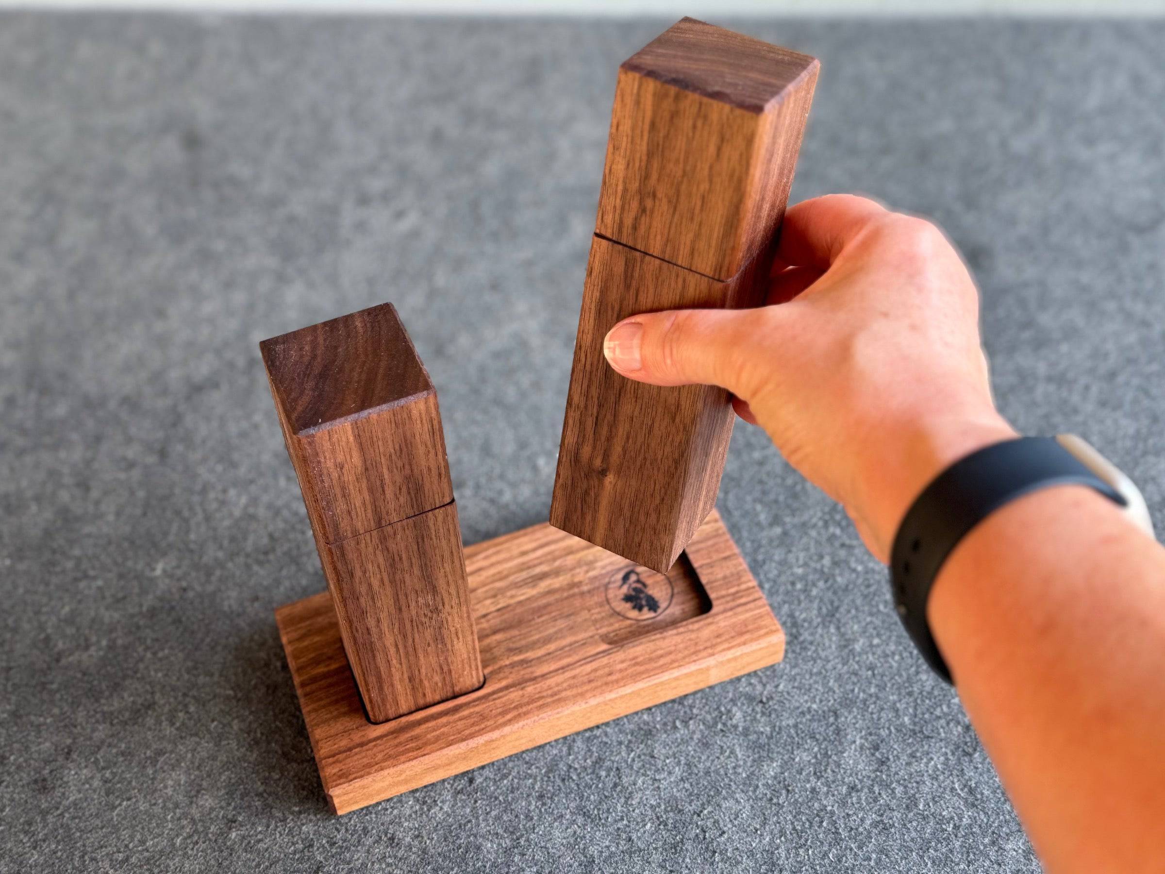 Hand hebt eine Nussbaum Salzmühle von einem Mühlenteller. Sichtbar wird das Spessarbrett Logo.