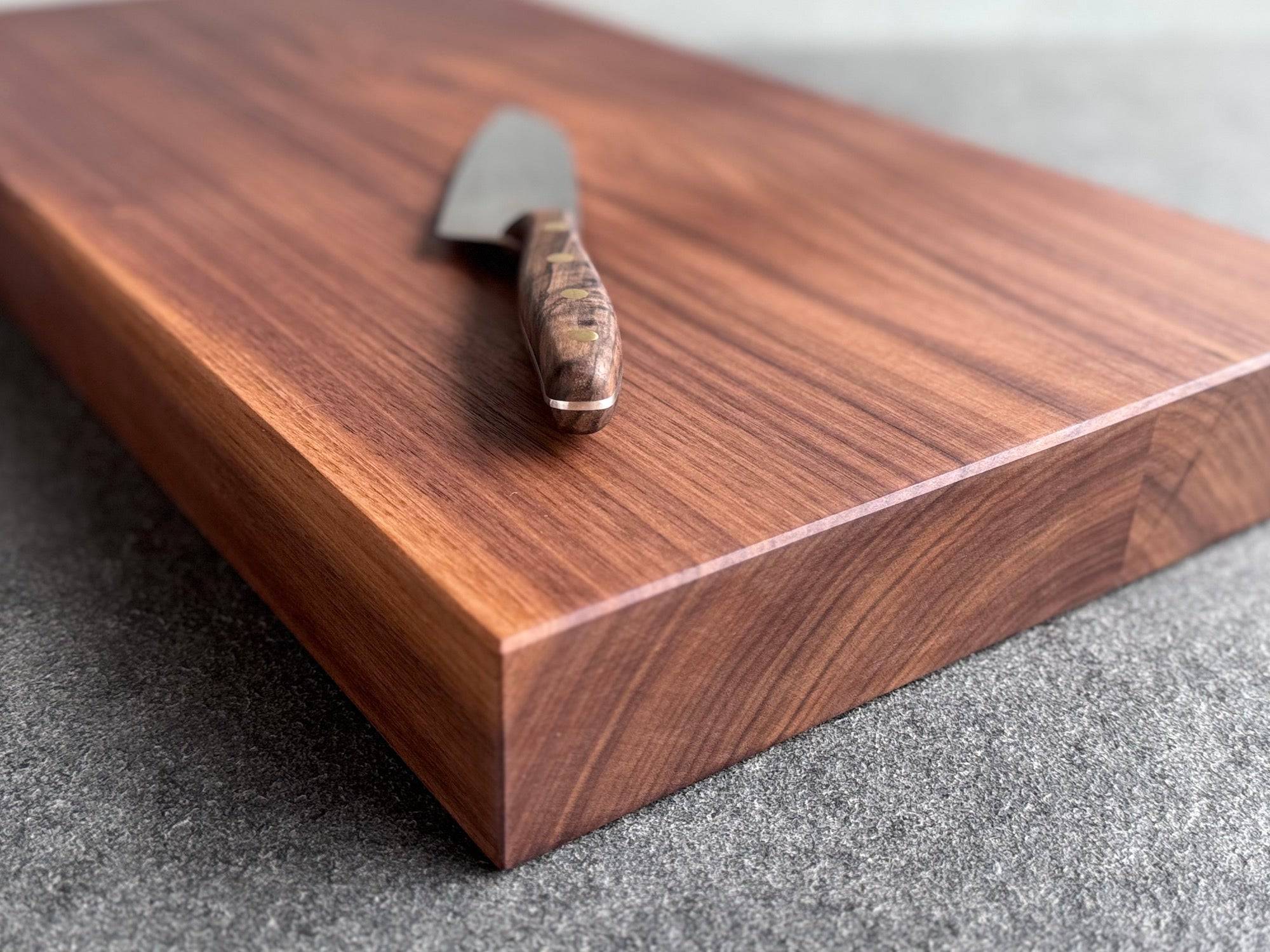Nussbaum Schneidebrett auf einer Granit Platte liegend. Darauf liegt ein Santoku Messer.