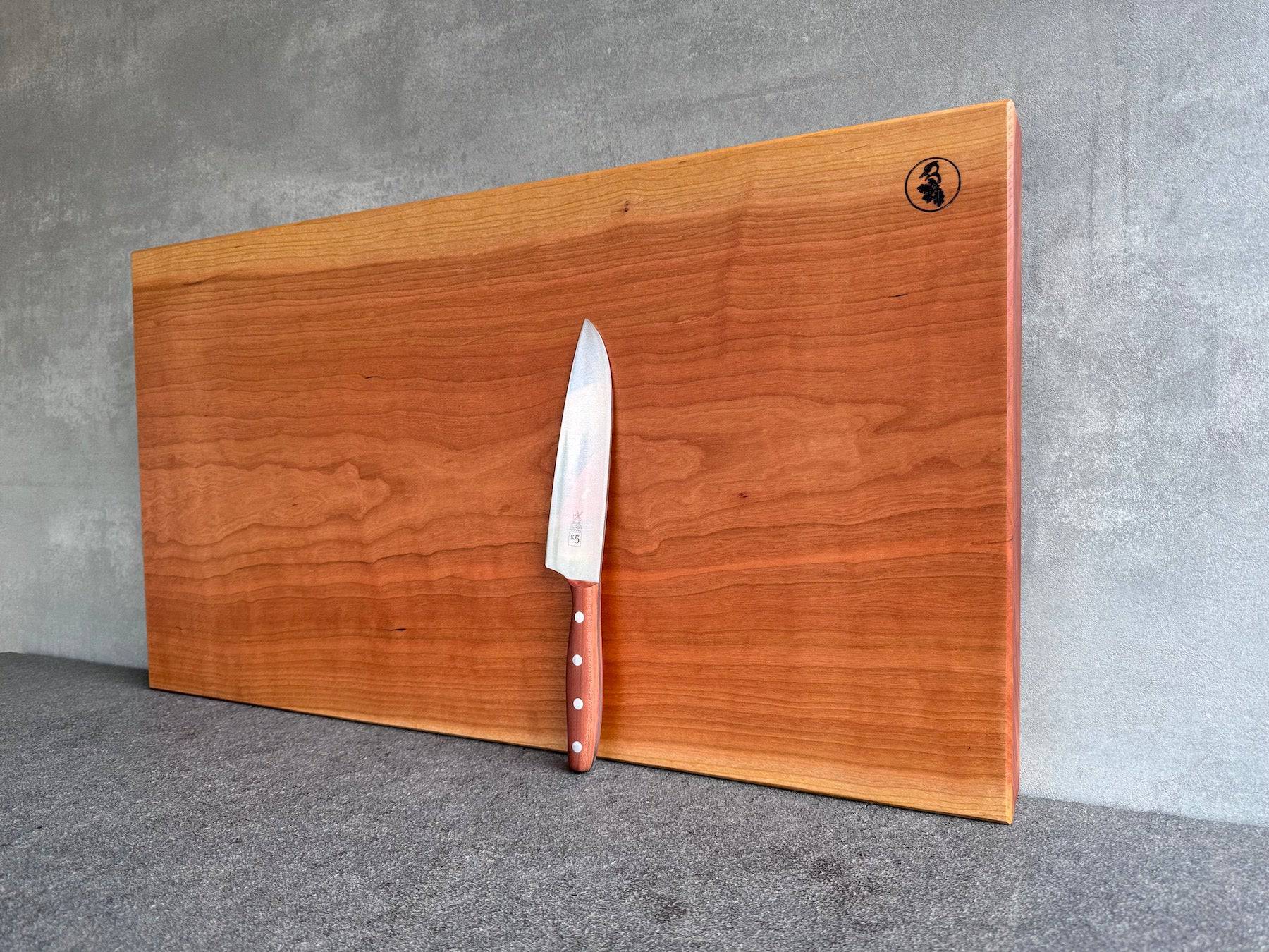 Seitliche Ansicht der Jahresringe bei einem Schneideblock aus Kirschbaum. Dekoriert mit einem Windmühlenmesser K5 mit Pflaume-Griff.