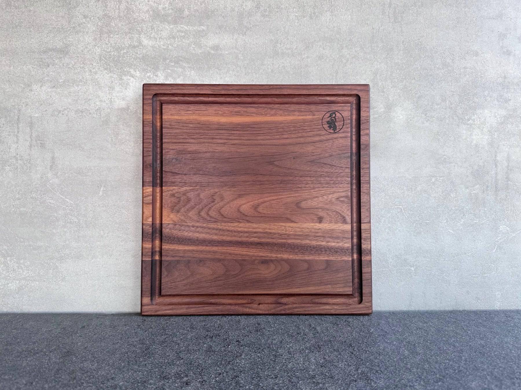 Tolle Maserung eines quadratischen Saftrillenbrettes in Nussbaum an einer Betonwand.