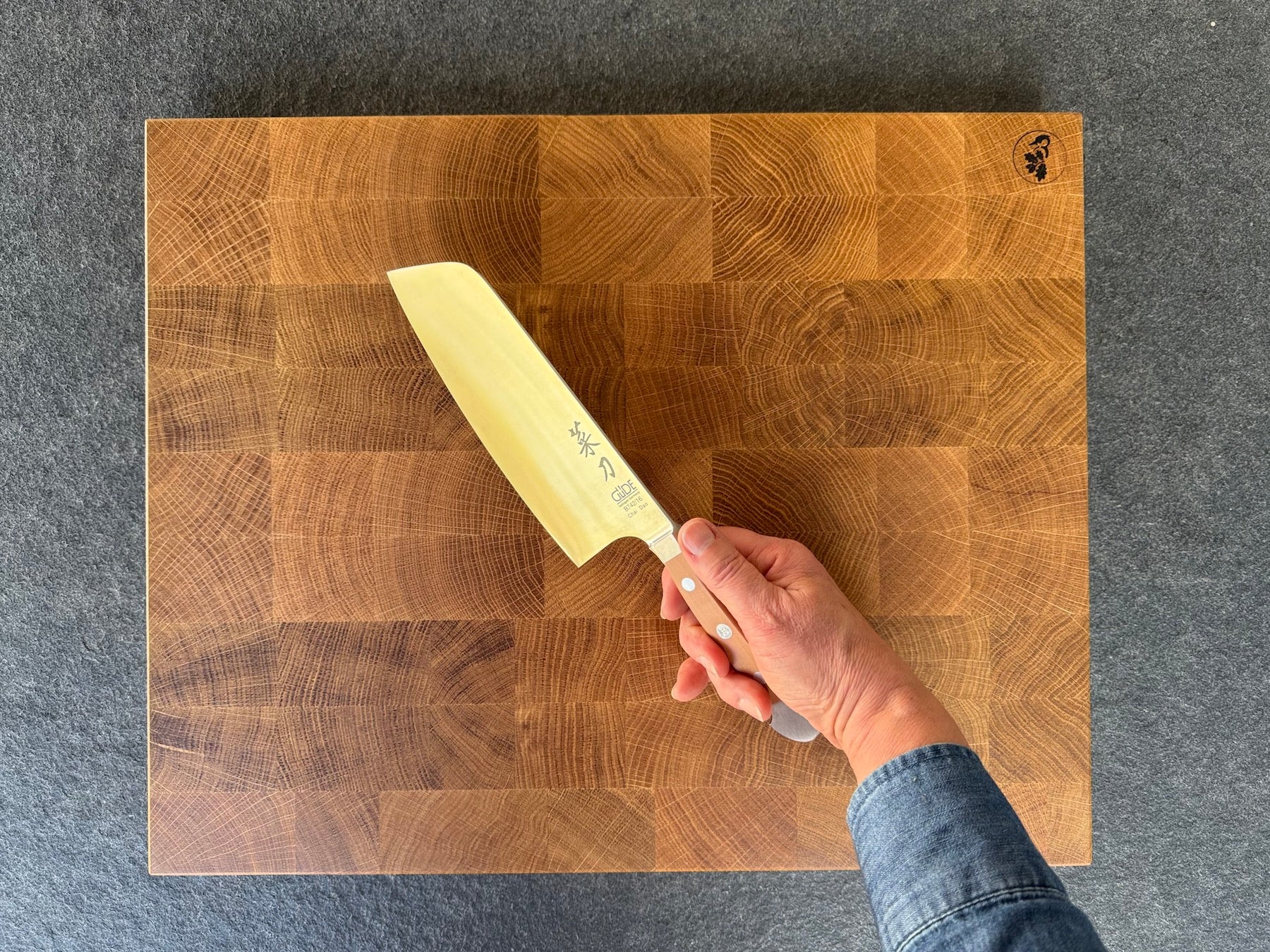 Frau hat ein Chinesisches Kochmesser von Güde in der Hand. Im Hintergrund ein Stirnholzblock in Eiche.