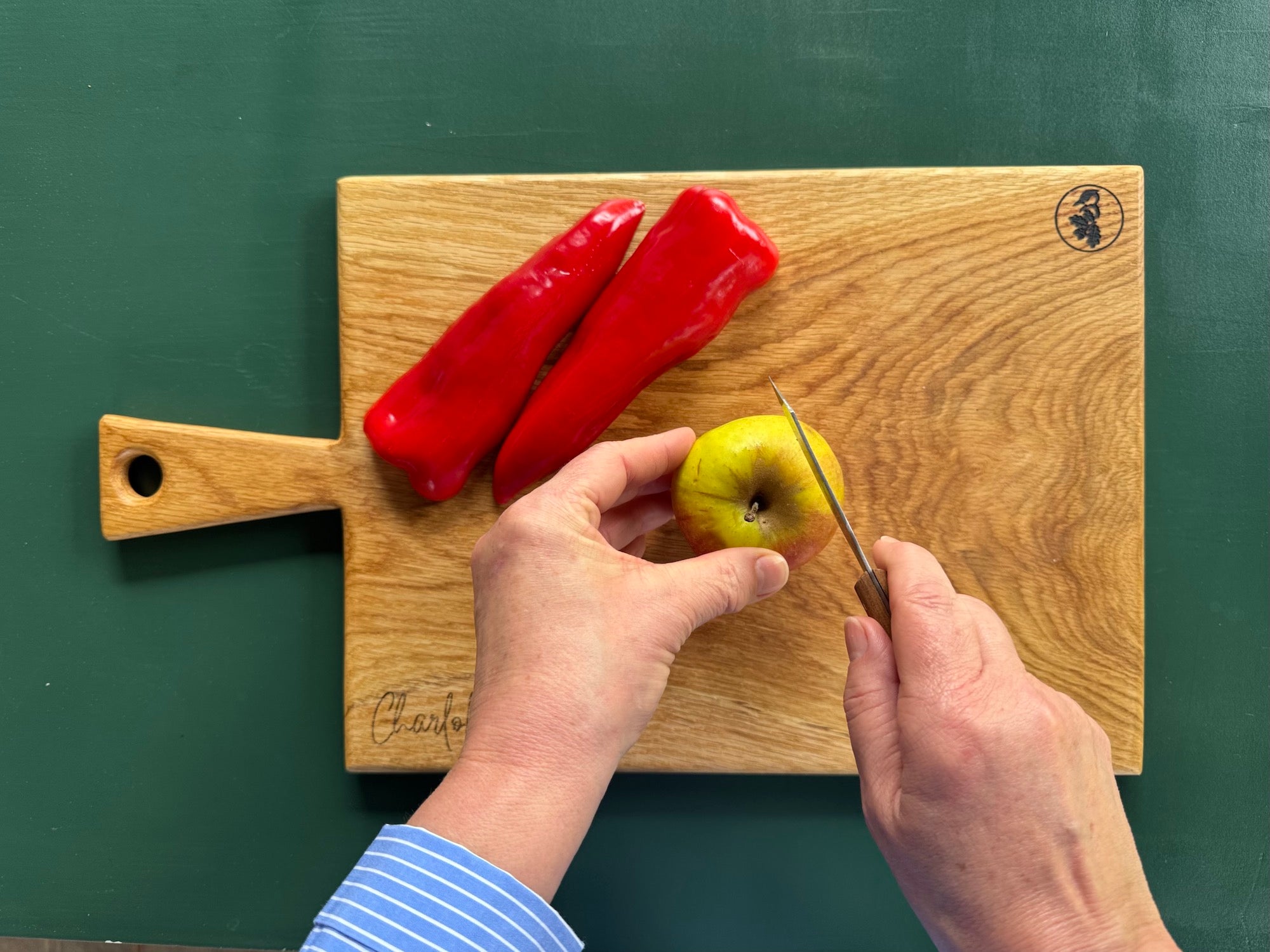 Hände halten ein Mini Gemüsemesser und schneidet einen Apfel auf einem Eichebrett von Spessartbrett.