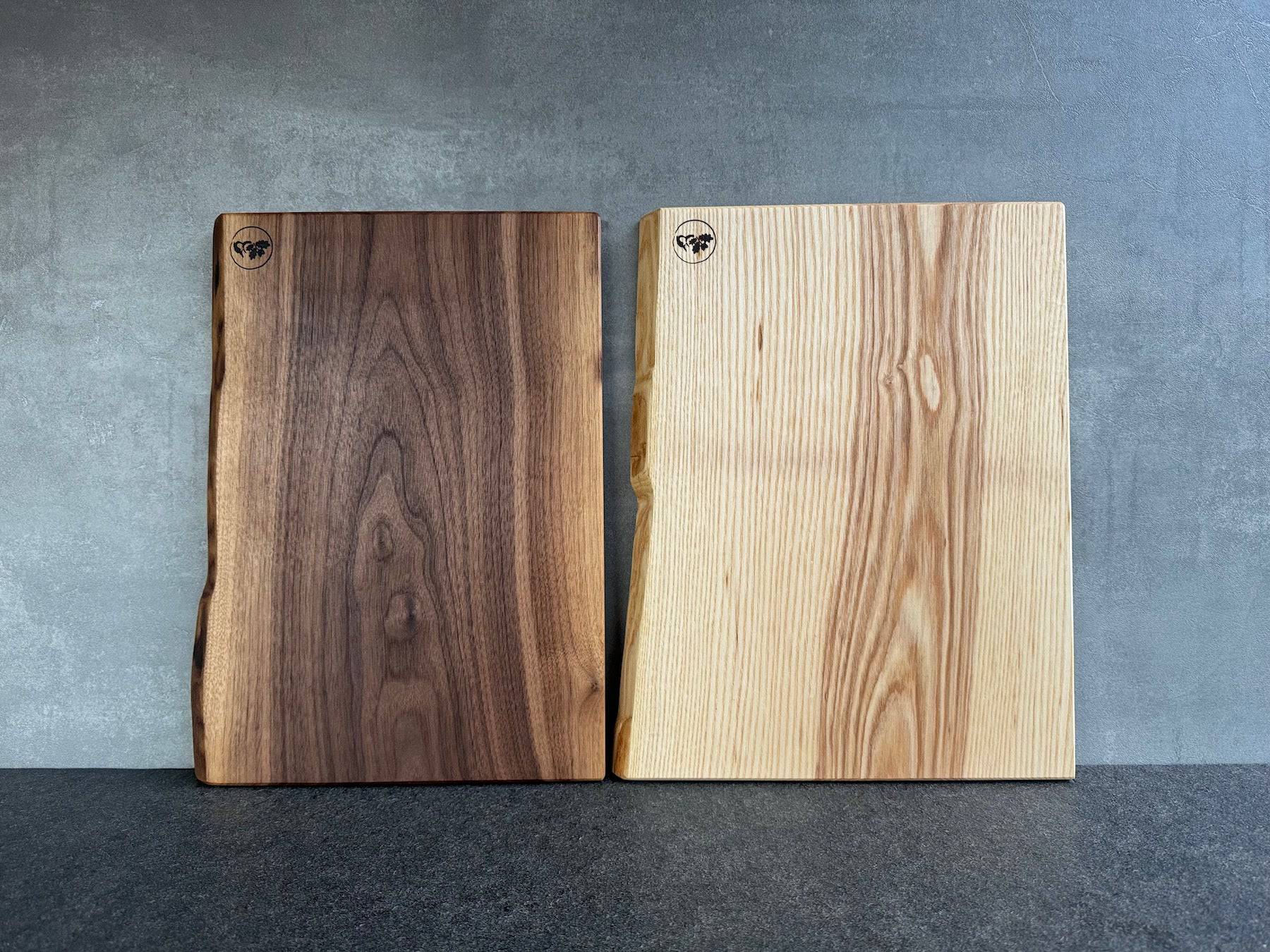 2 Brotbretter aus einem Stück Nussbaum und Vogelbeere an einer Betonwand.