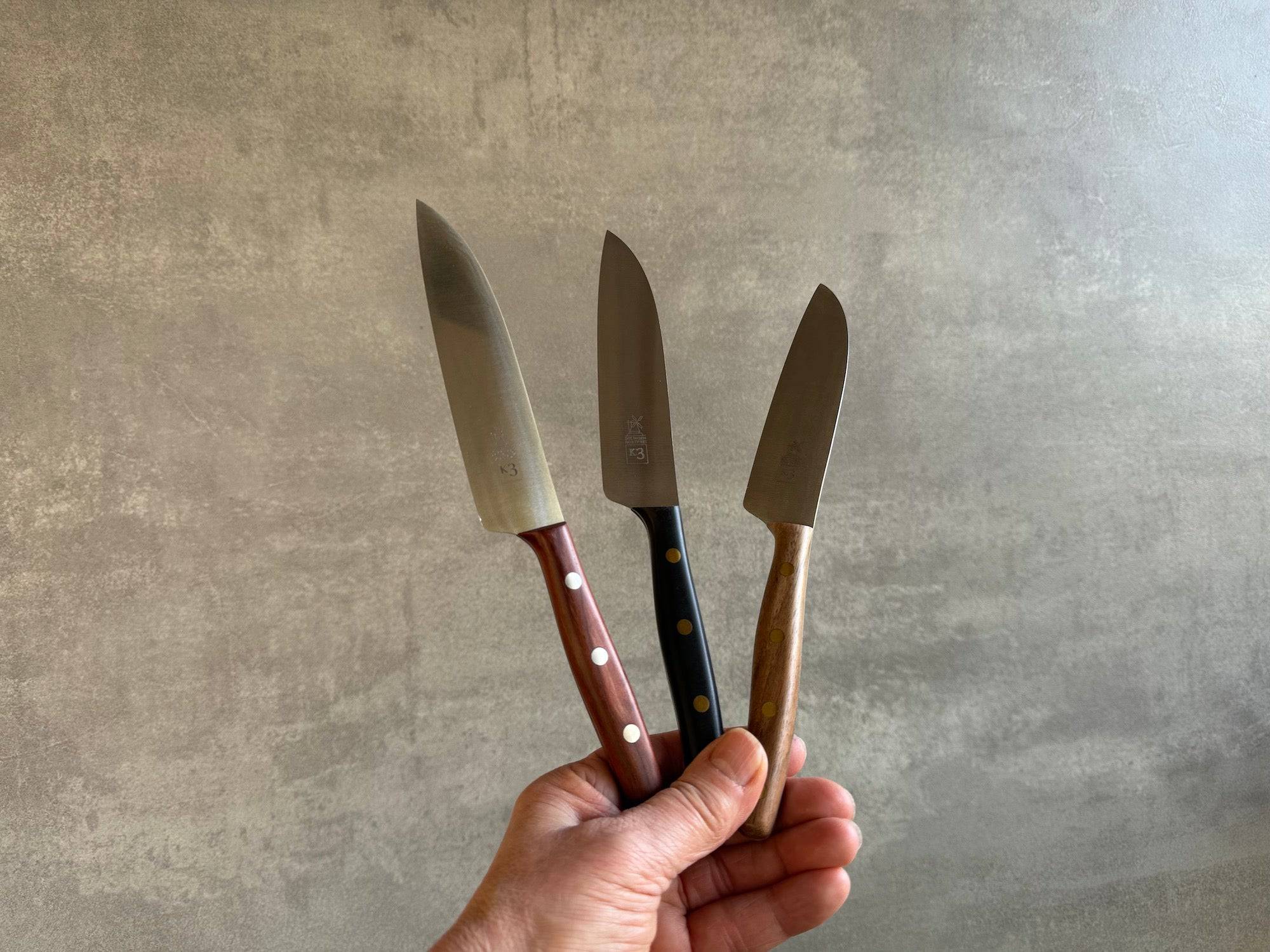 Eine Hand hält 3 Windmühlenmesser K3 mit 3 verschiedenen Holzgriffen in der Hand.