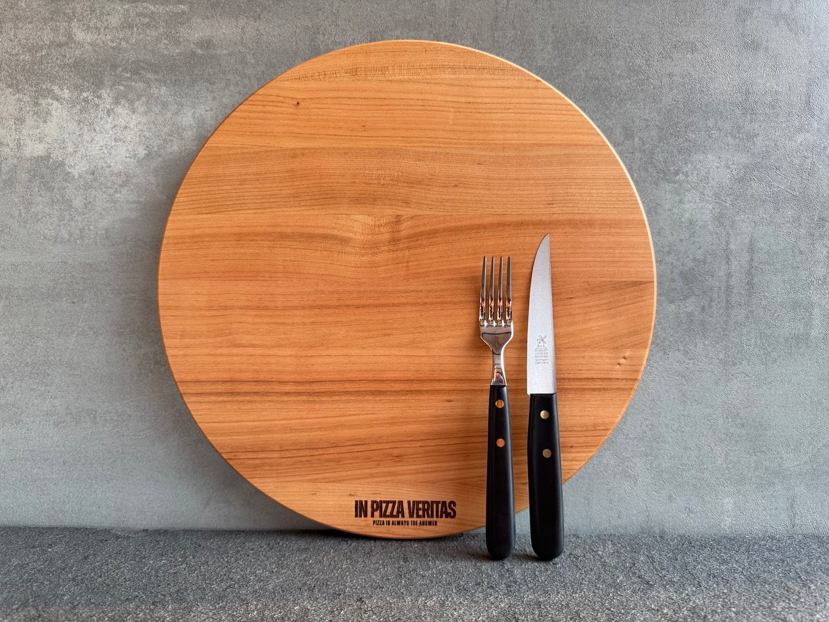 Handgefertigtes Pizzabrett aus massivem Kirschbaum, rund, ohne Griff.
Mit Pizzabesteck von Windmühlenmesser.
