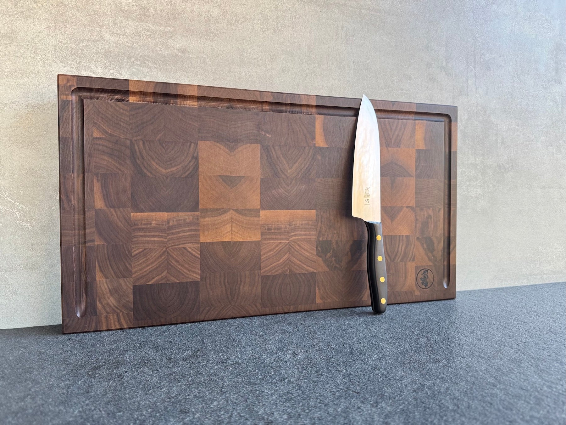 Schneideblock aus Nussbaum Stirnholz mit Saftrille und Griffmulden. Dekoriert mit einem K5 Kochmesser.