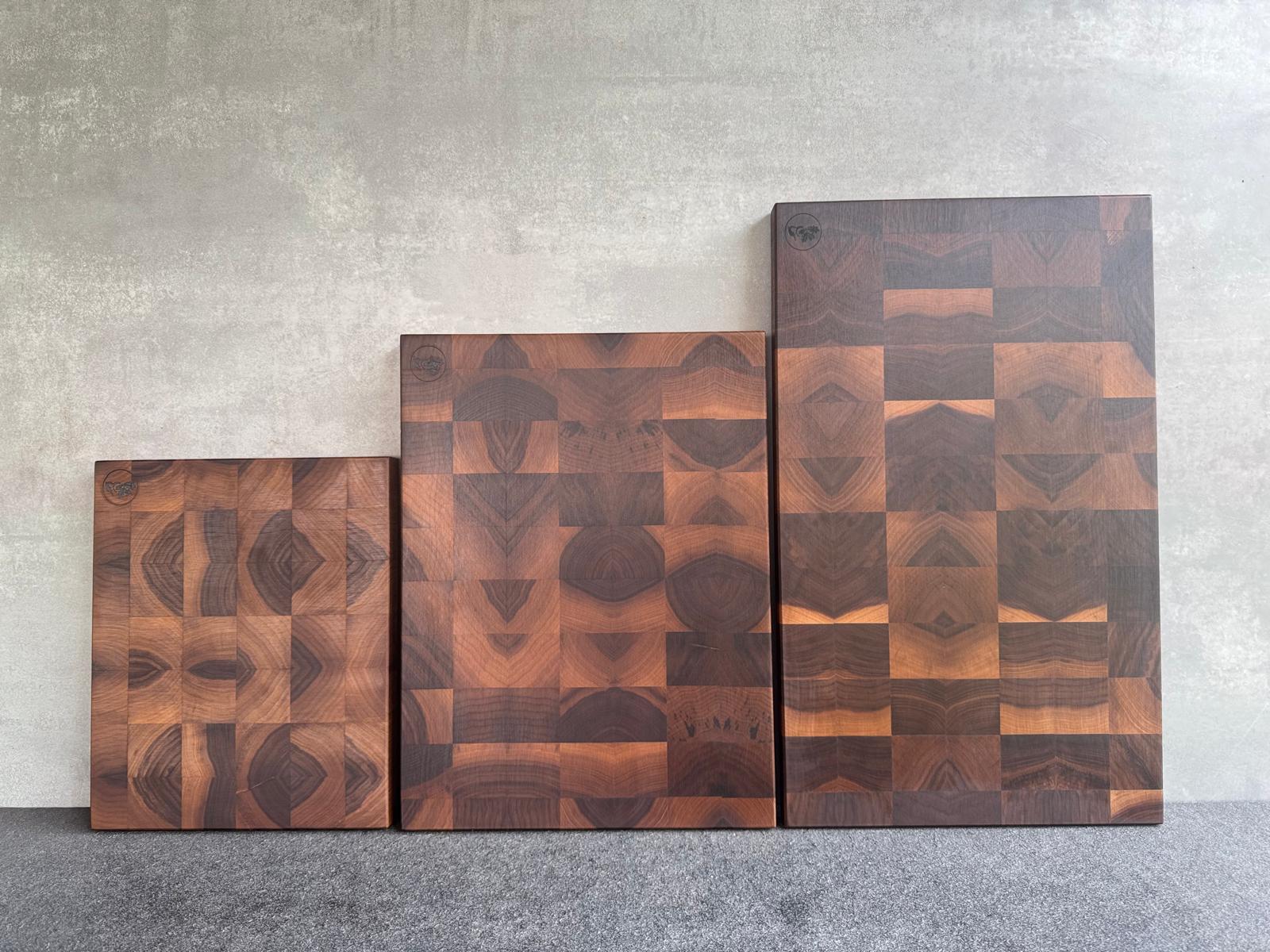 3 verschieden große Nussbaum Hirnholz Schneidebretter an einer Betonwand aufgestellt.