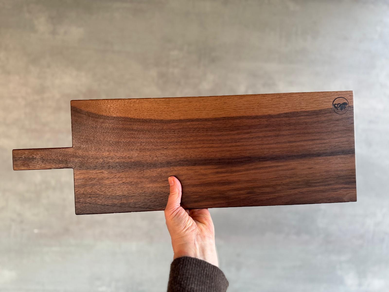 In der Hand ein 60 cm langes Servierbrett aus einem Stück Nussbaum