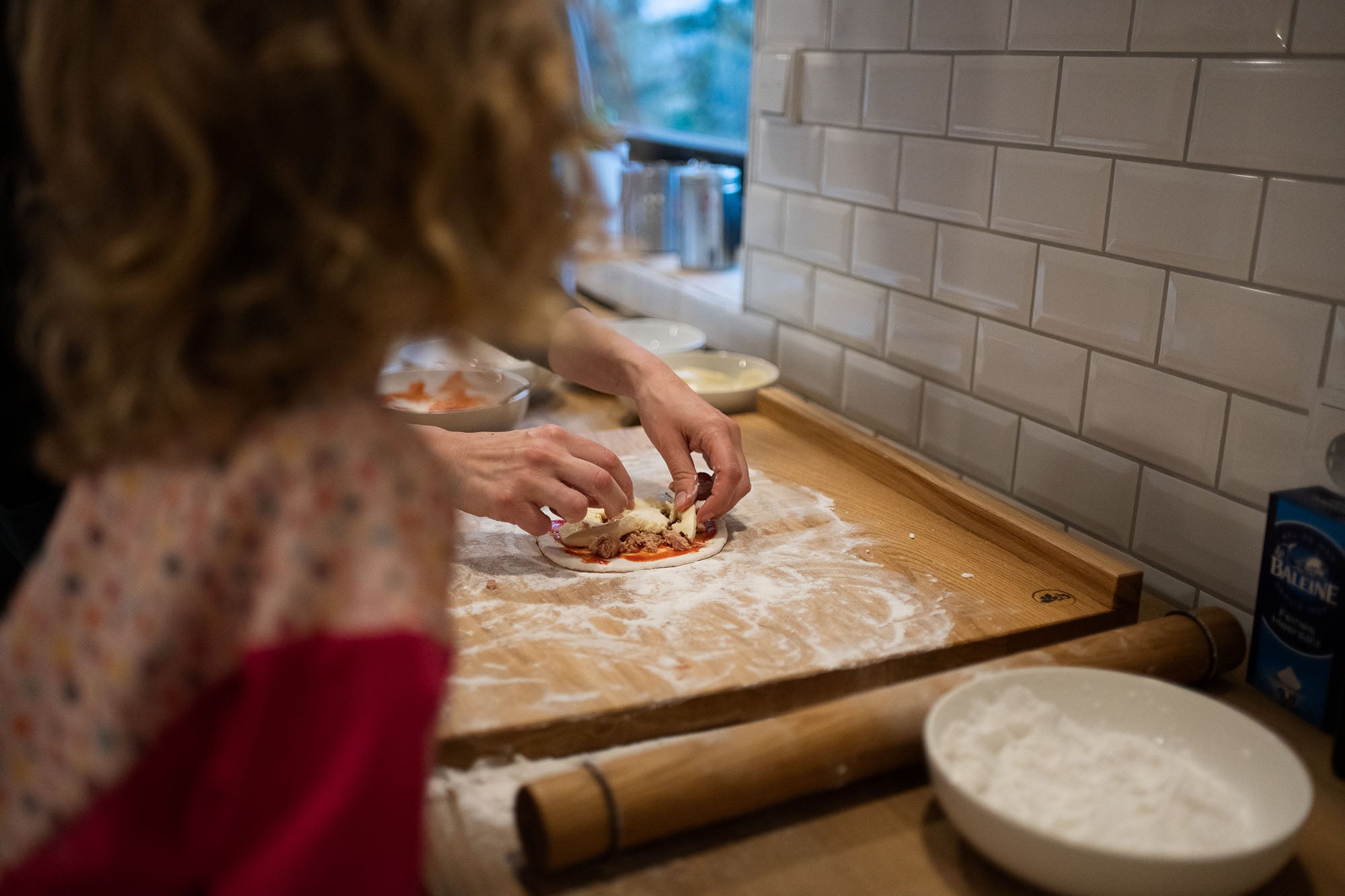 Pizza wird auf einem Holzbrett zubereitet und Kind schaut zu