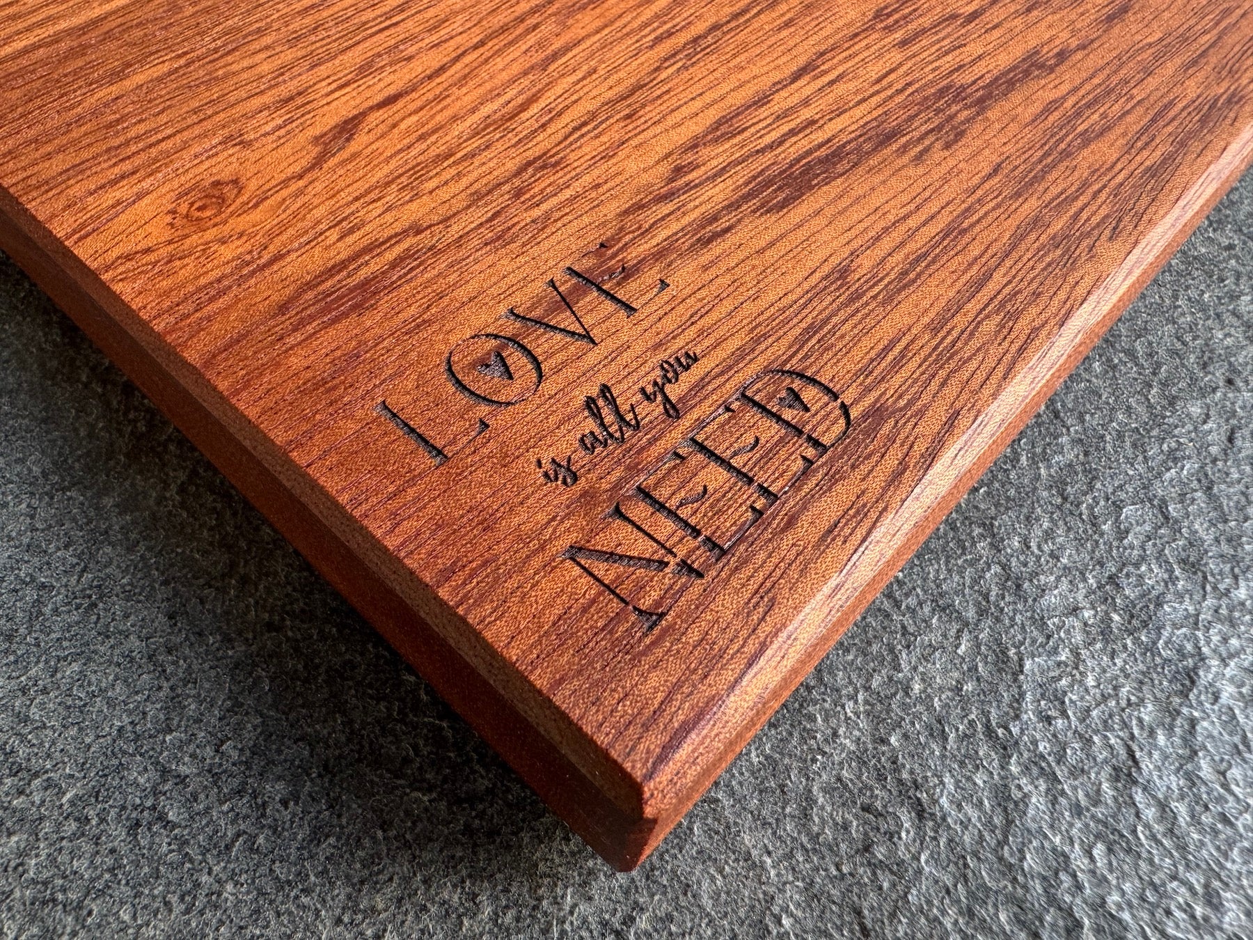 Personalisierte Gravur „Love is all you need“ bei einem Edelholzbrett.