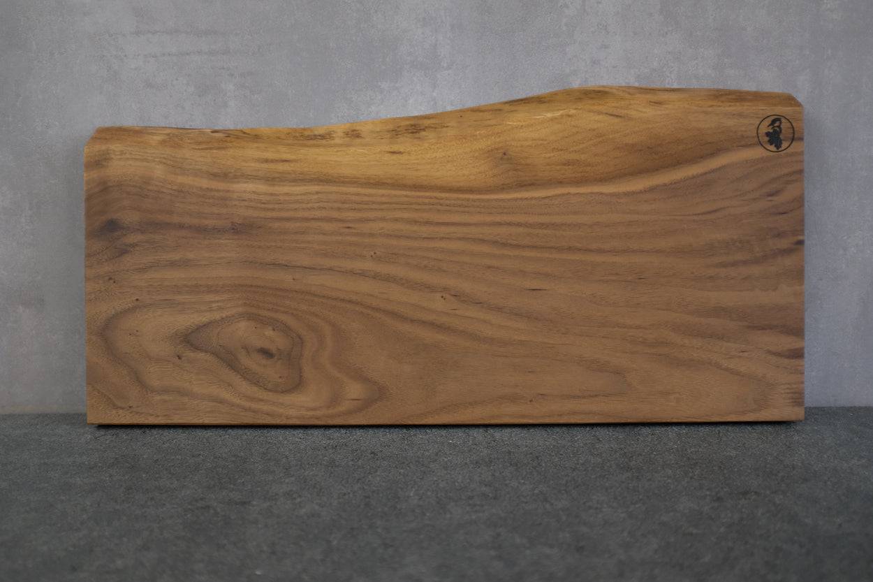 Handgemachtes Vollholz Schneidebrett aus einem Stück Nussbaum, angelehnt an einer Betonwand. Tolle Maserung.