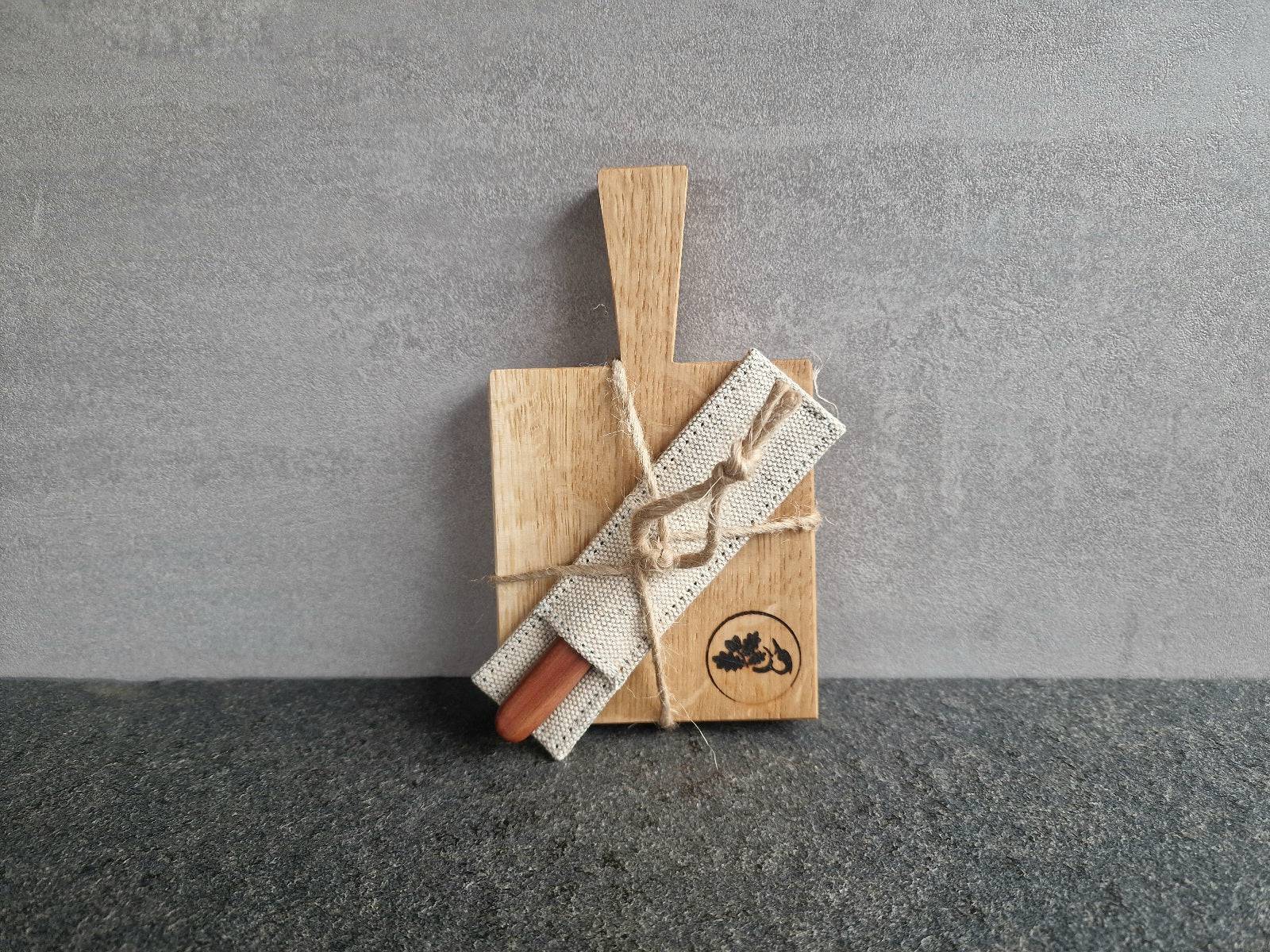 Kleines Eichenbrett für Kräuterbutter mit einem Beilegemesser im Leinen-Etui an einer Betonwand.