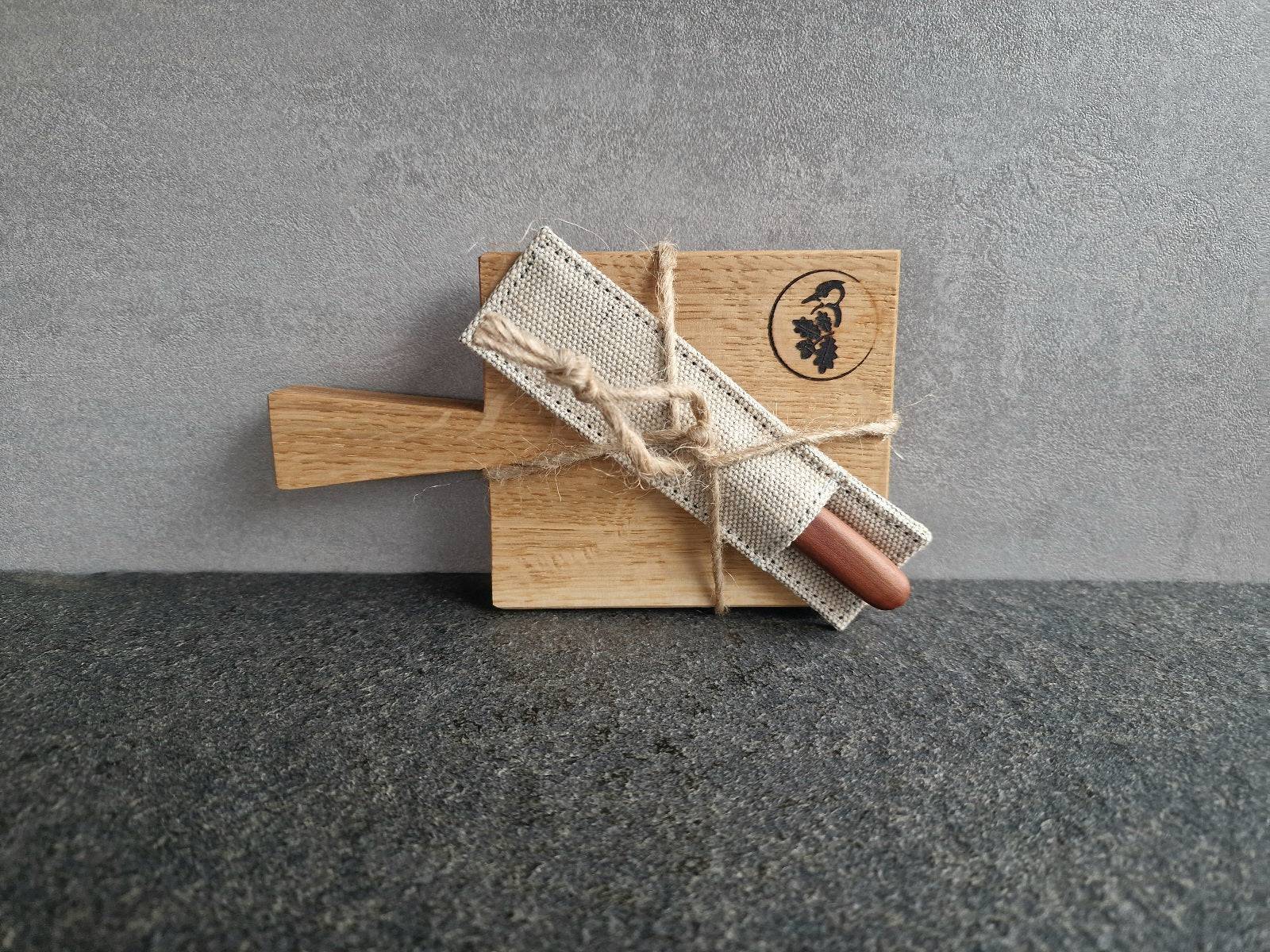 Amuse Bouche Eichenbrett an einer Betonwand mit einem kleinen Buttermesser im Leinen-Etui verpackt.