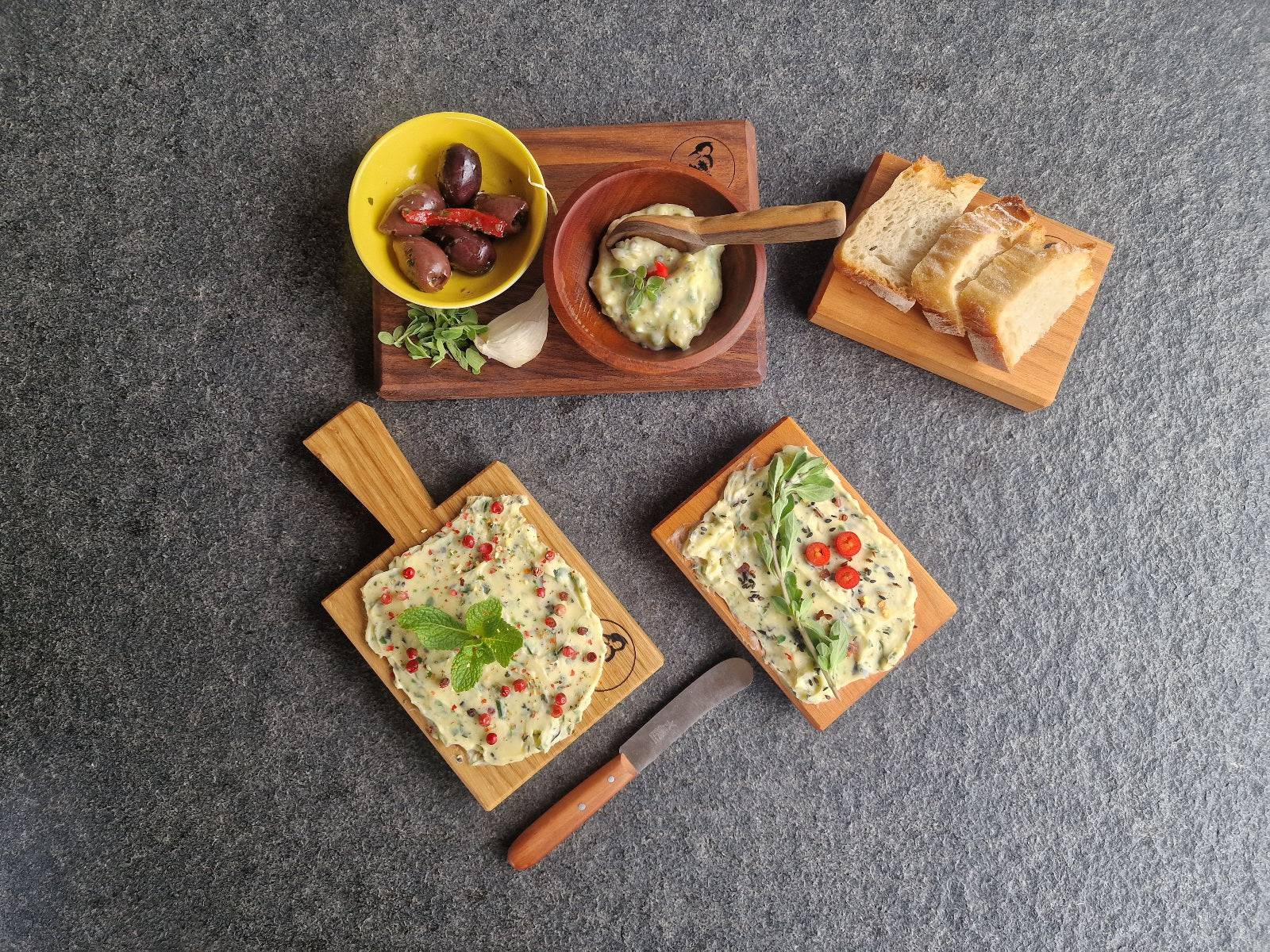 2 Butterboard Gerichte und Dinkelbrot Scheiben auf kleinen Holzbrettern angerichtet. Oliven und Kräuterbutter in einer Schale.