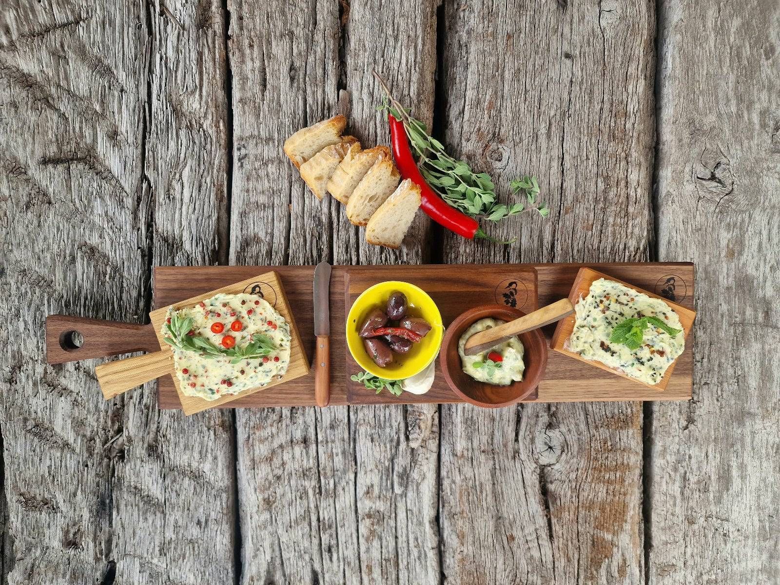Edeles Tapasbrett Aus Nussbaum mit kleinen Butterboard Gerichten, Oliven, Brot und Kräuterbutter angerichtet. In der Mitte ein Windmühlenmesser Butter Buckels Buttermesser.
