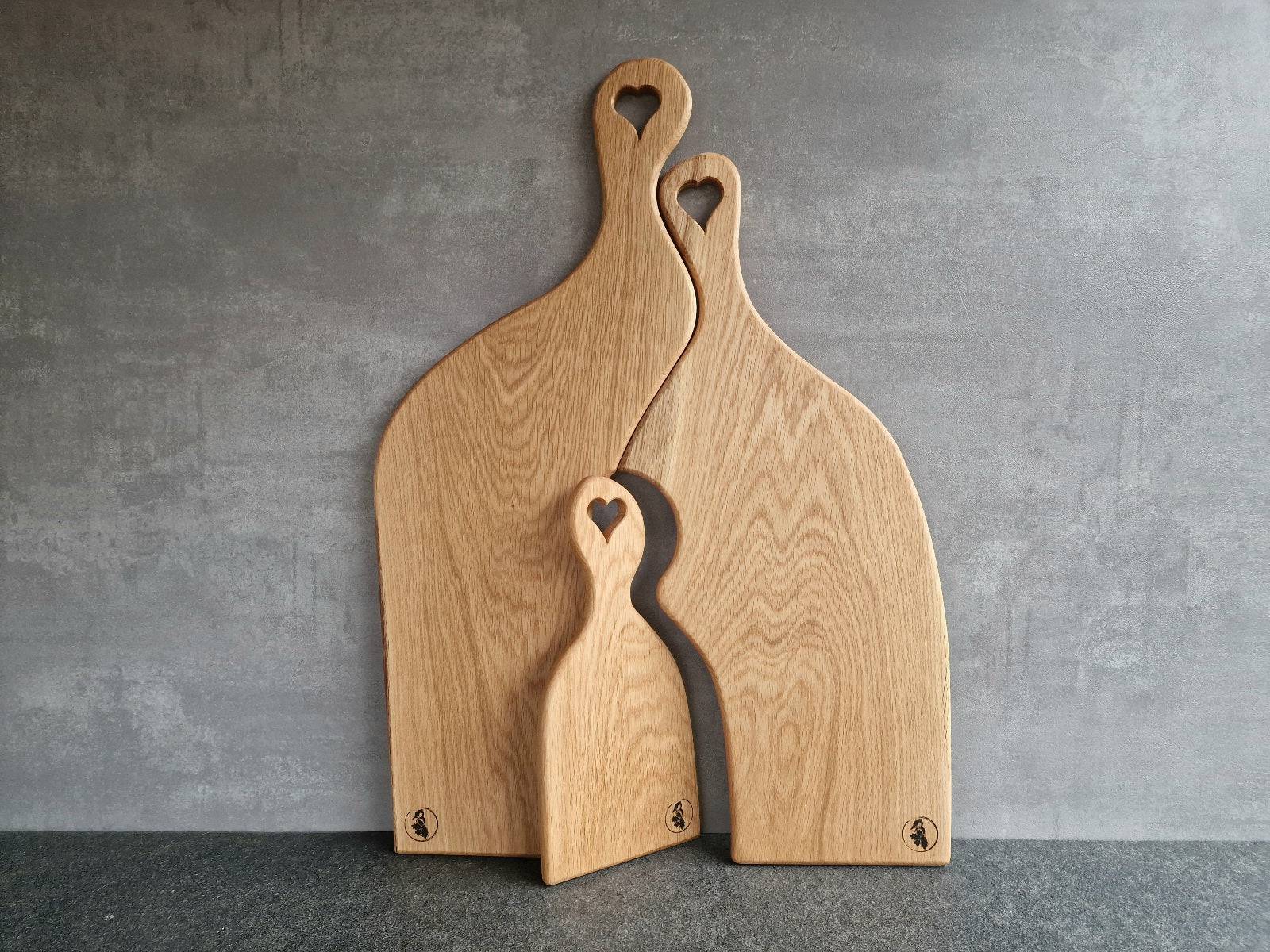 Papa, Mama, Kind. Familienbrett, 3-teilig, aus massiver Eiche. 3 Servierbretter mit Herz im Stiel an einer Betonwand.