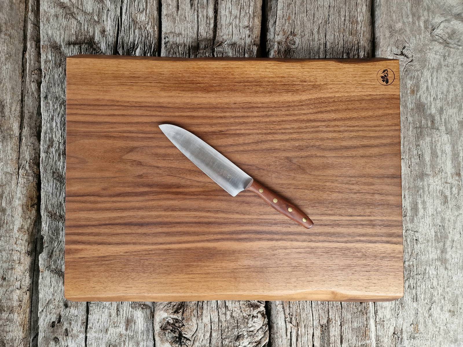 Dicker Schneideblock aus einem Stück Nussbaum liegt auf alten Eichenbalken. Dekoriert mit einem Kochmesser K5 mit Walnuss-Griff von Windmühlenmesser.