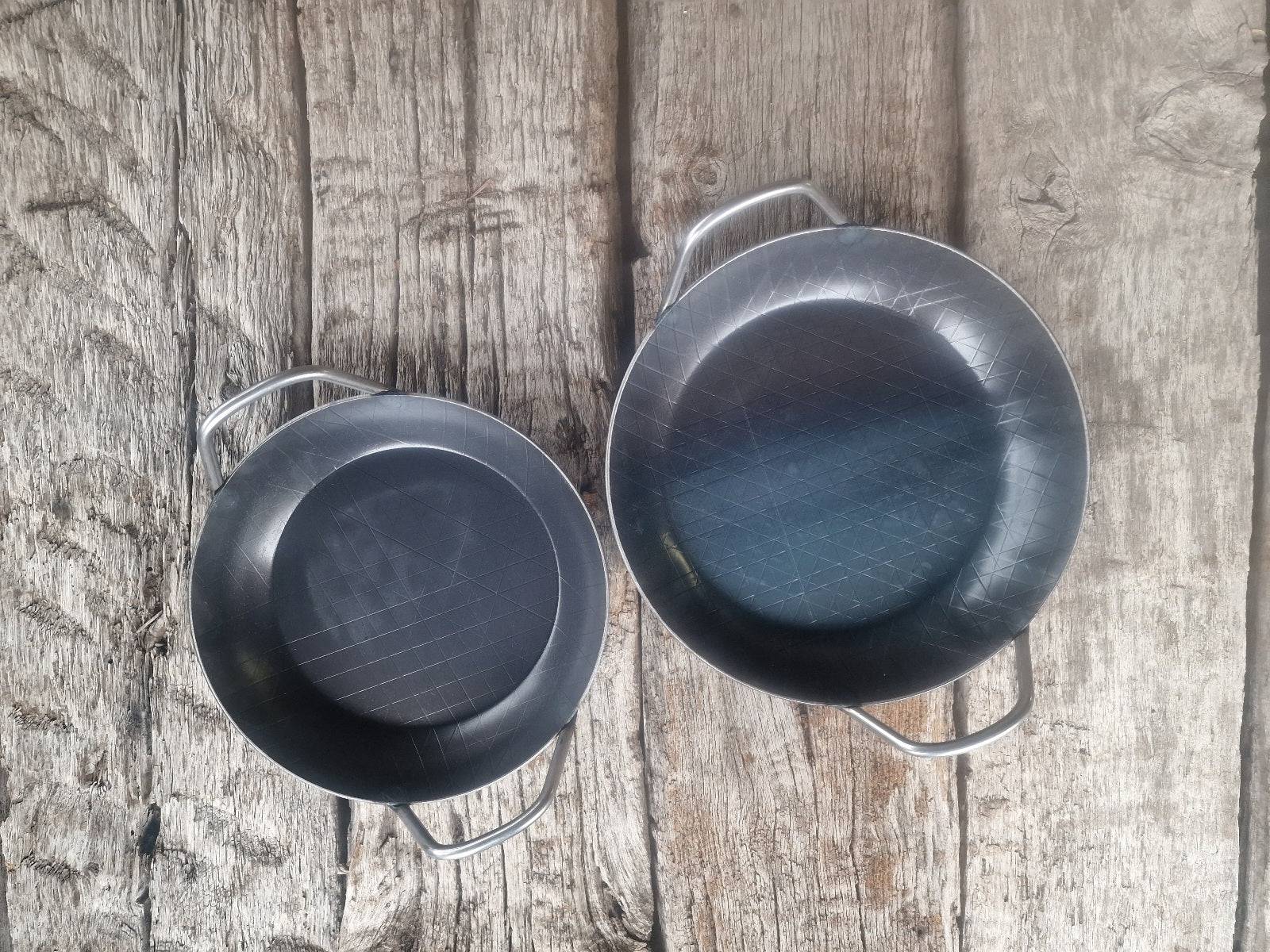 2 Servierpfannen aus Eisen mit 2 Griffen im Vergleich nebeneinander.