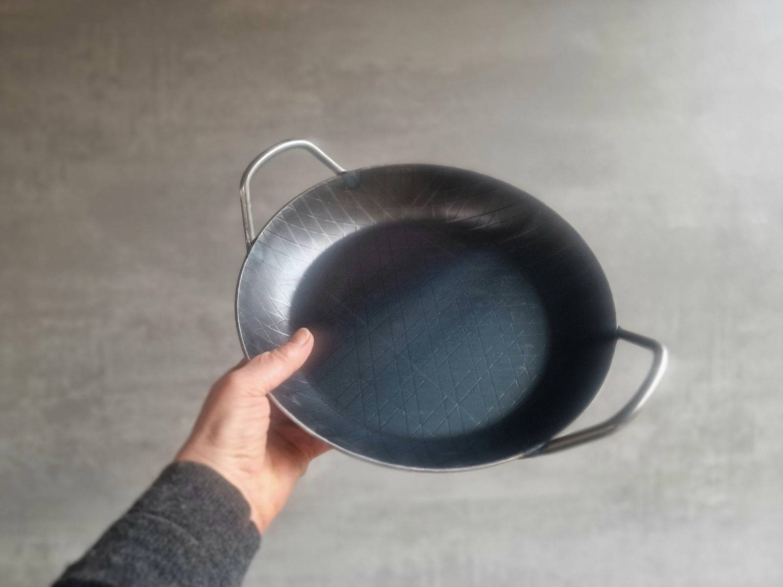 Eine Hand hält eine Eisenpfanne in die Höhe.