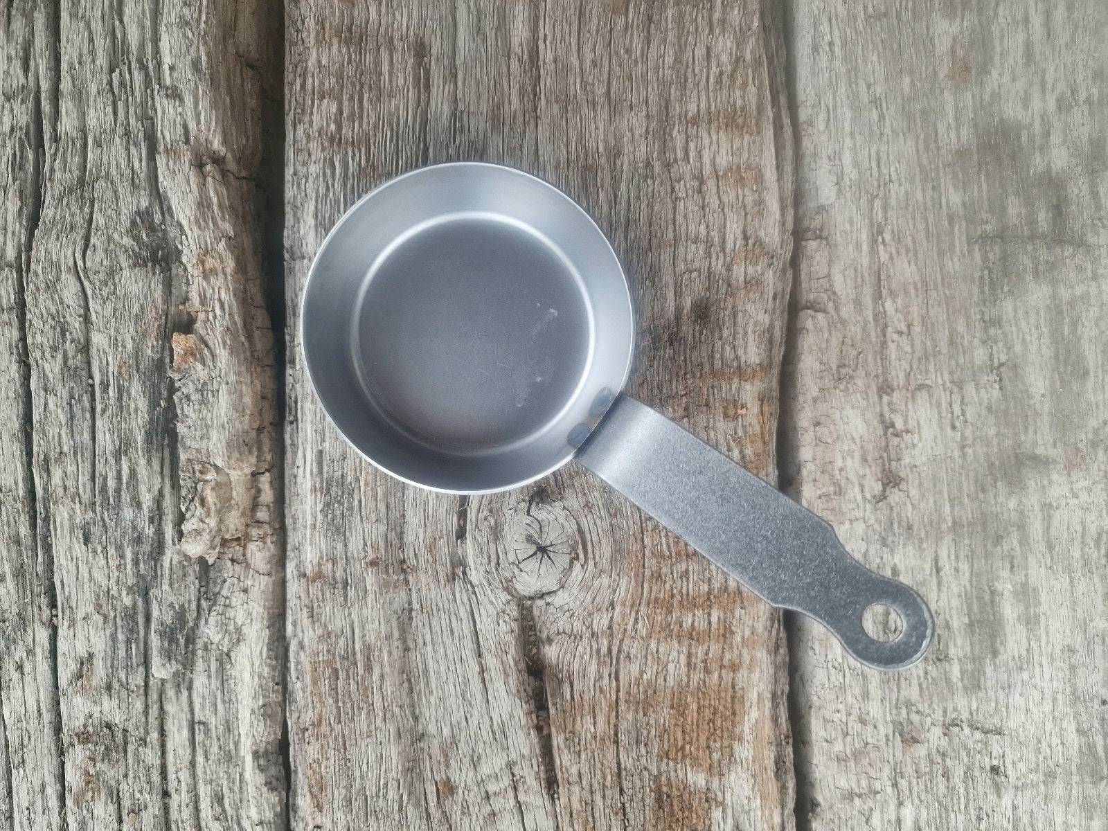 Mini Eisenpfanne mit Stiel auf historischen Eichenbalken.