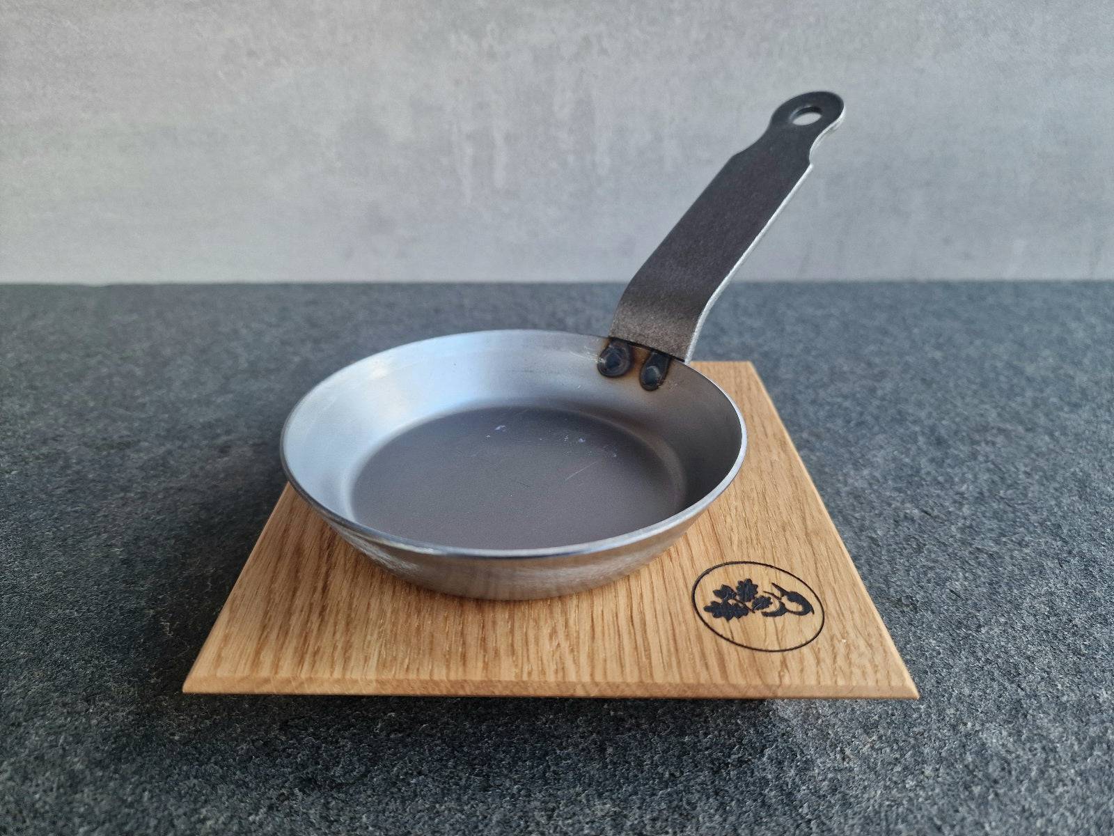 Kleine Tapas Eisenpfanne auf einem Eichenholz Topfuntersetzer von Spessartbrett.