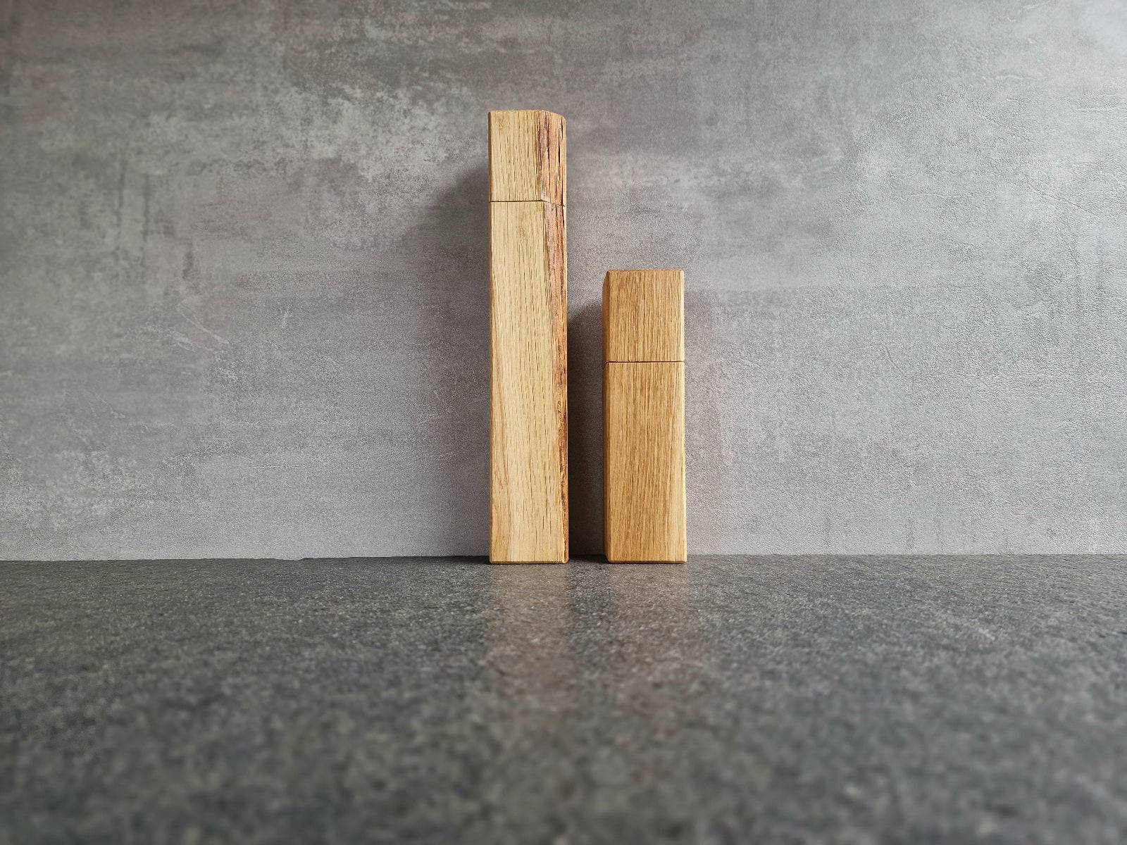 28 cm Pfeffermühle und 18 cm Salzmühle aus massiver Eiche an einer Betonwand.
