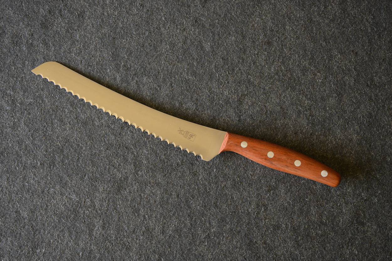 Windmühlenmesser Brotbeidhänder für Linkshänder und Rechtshänder mit Pflaumegriff auf einer Steinplatte liegend.