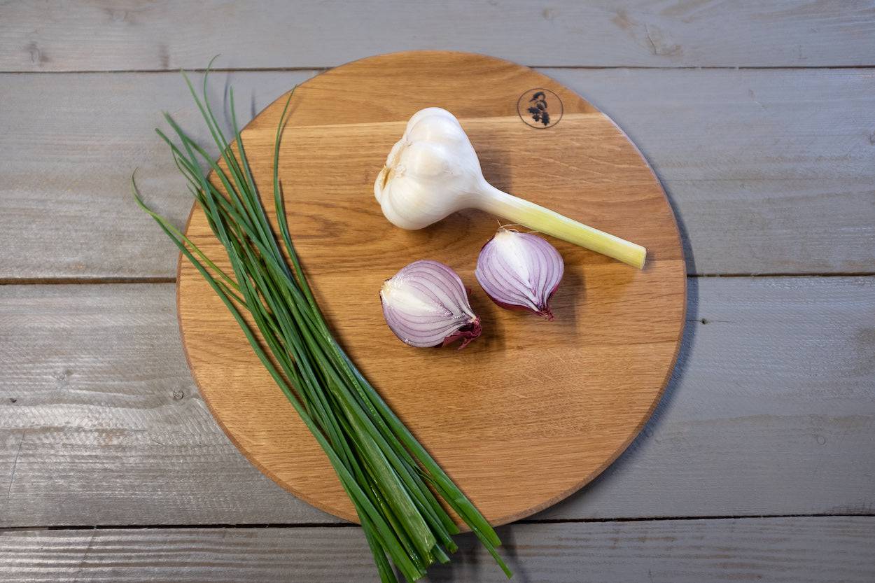 Rundes Schneidebrett aus Eiche mit Knoblauch, Zwiebeln und Schnittlauch von oben