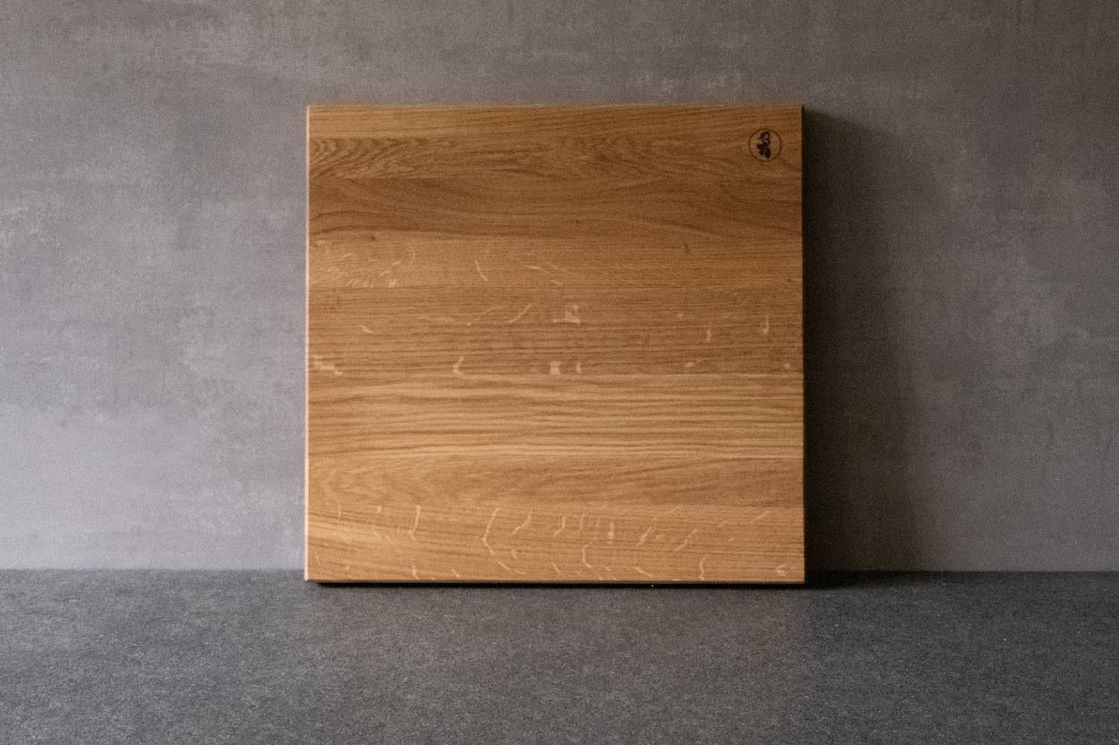 Quadratischer Schneideblock aus Eiche massiv. An einer Betonwand angelehnt.