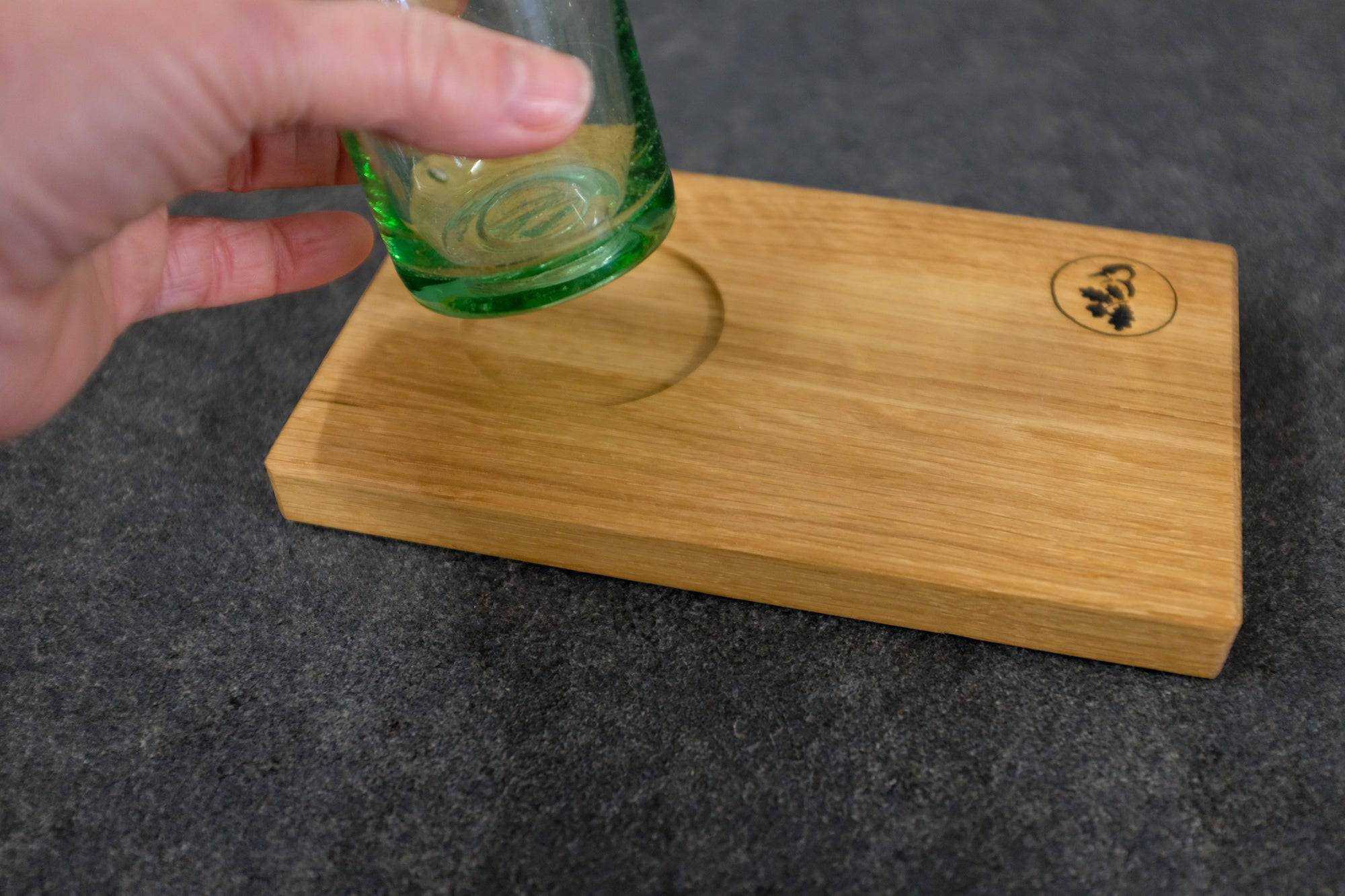 Grünes Trinkglas mit der Hand gehoben auf einem Eiche Holztablett "Karlstadt".