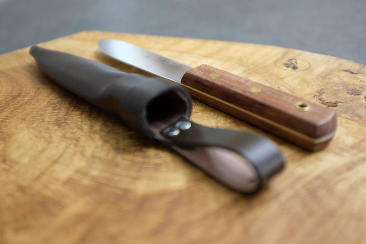 Lederscheide im Detail, nebenan das Matrosenmesser, auf einem Eichenbrett.