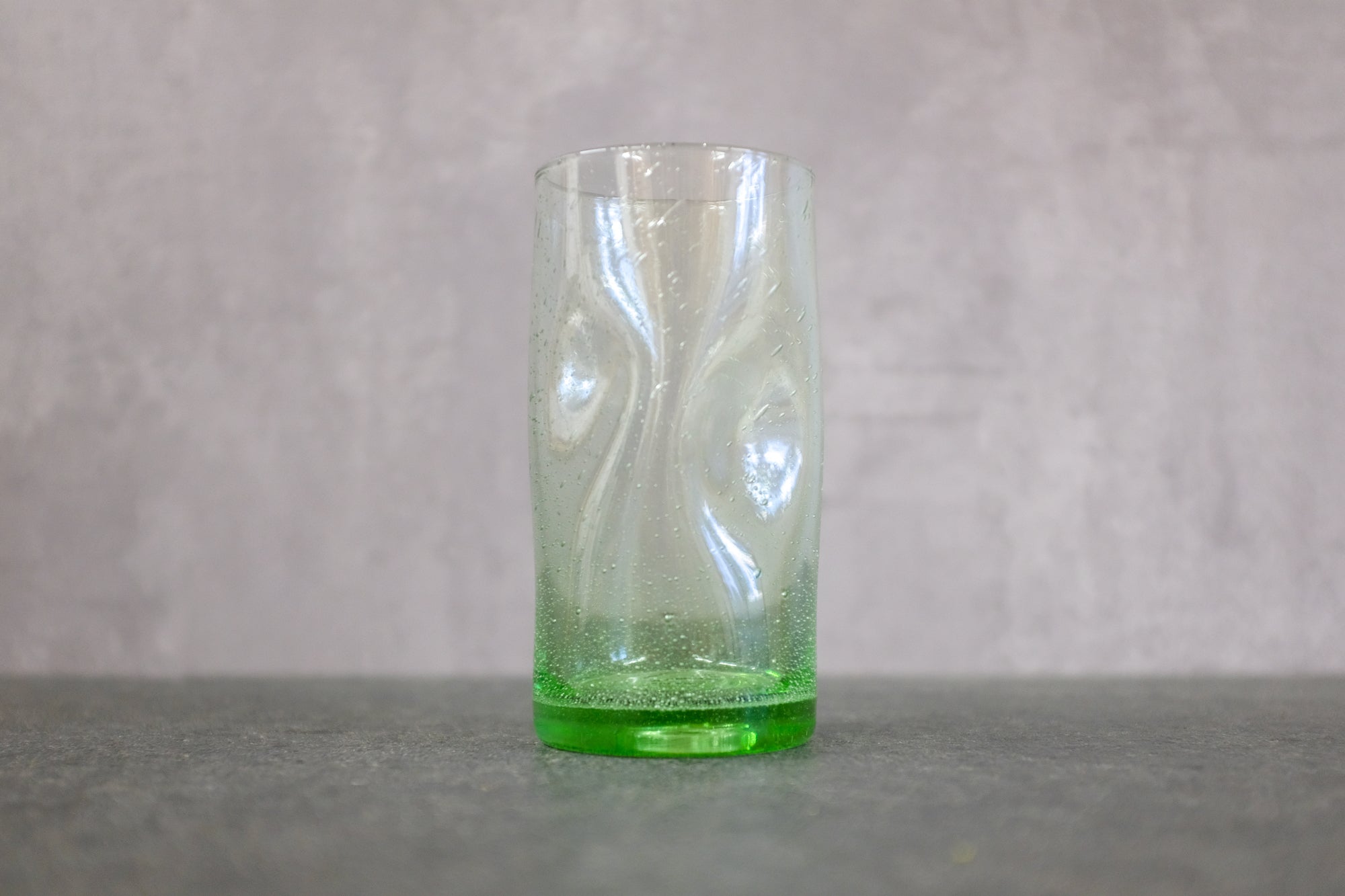 Dickwandiges Wasserglas mit Griffmulden auf einer Steinplatte.