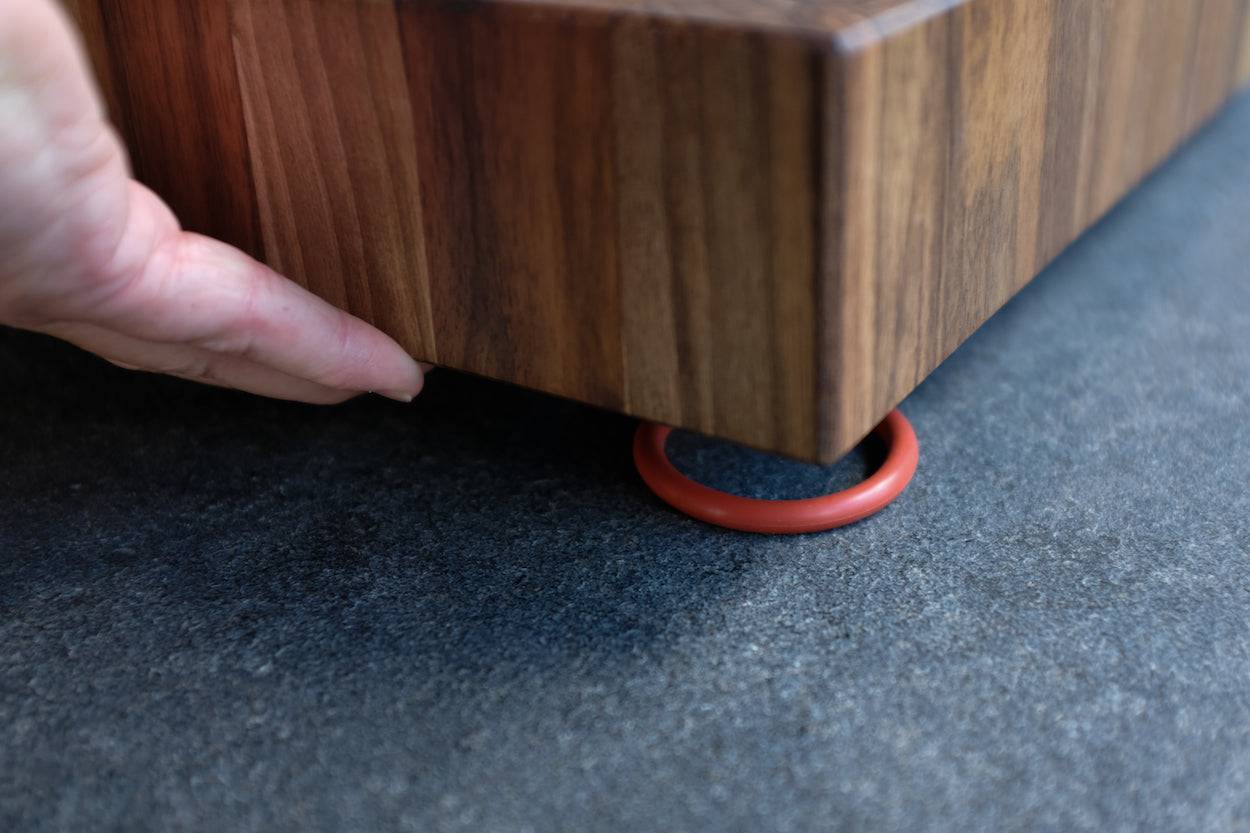 Hand hebt Schneidebrett Aus Nussbaum Hirnholz. Man sieht den Gummiring, auf dem der Block liegt.