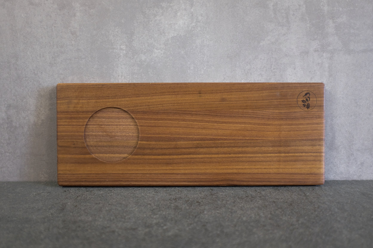 Holz Tablett in Nussbaum massiv mit einer Mulde für einen Pott an einer Betonwand angelehnt.