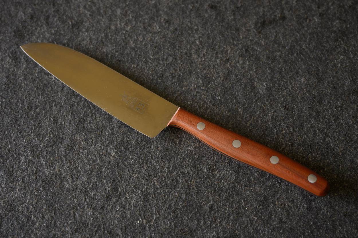 Kochmesser K3 mit einem Griff aus Pflaume auf einer Steinplatte liegend.