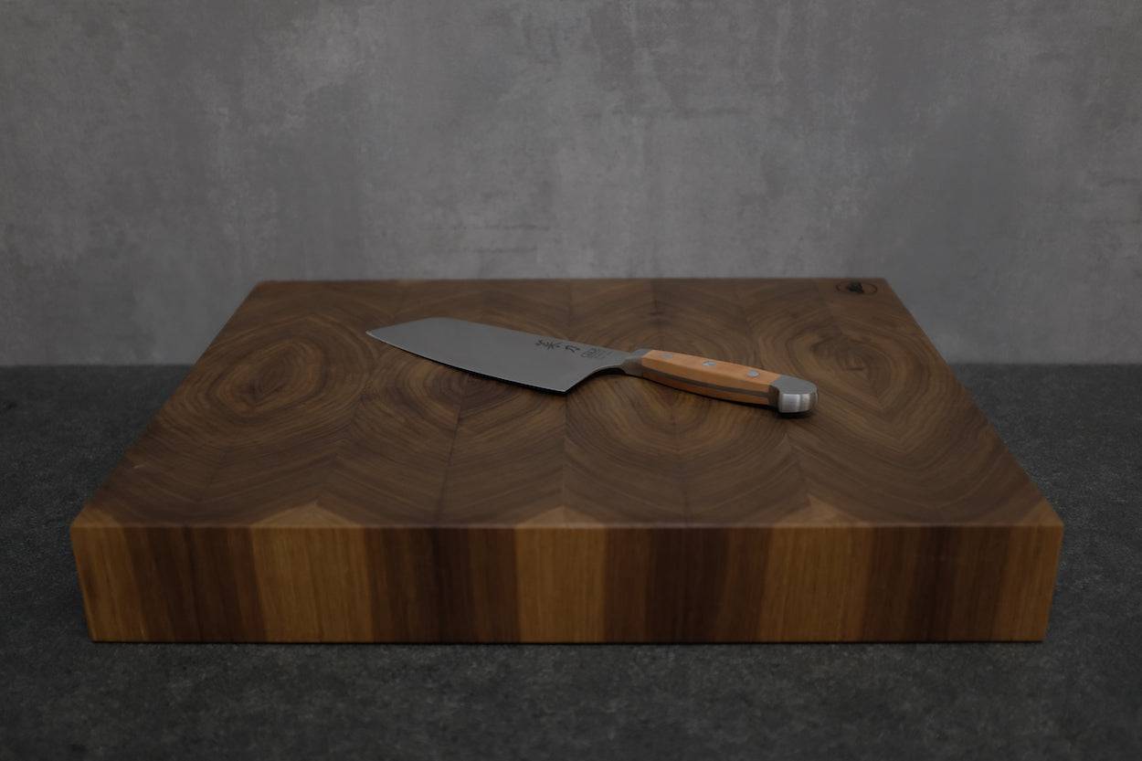 Du stehst vor deinem neuen Hirnholz Nussbaum Schneideblock mit wundervoller Maserung. Er liegt auf einer Steinarbeitsplatte mit einem Kochmesser von Güde.