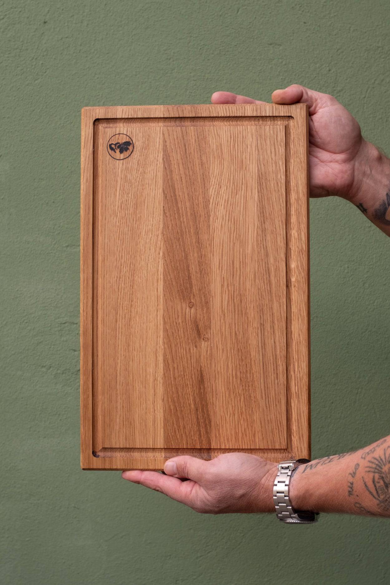 Schneidebrett mit Saftrinne in Händen frontal.