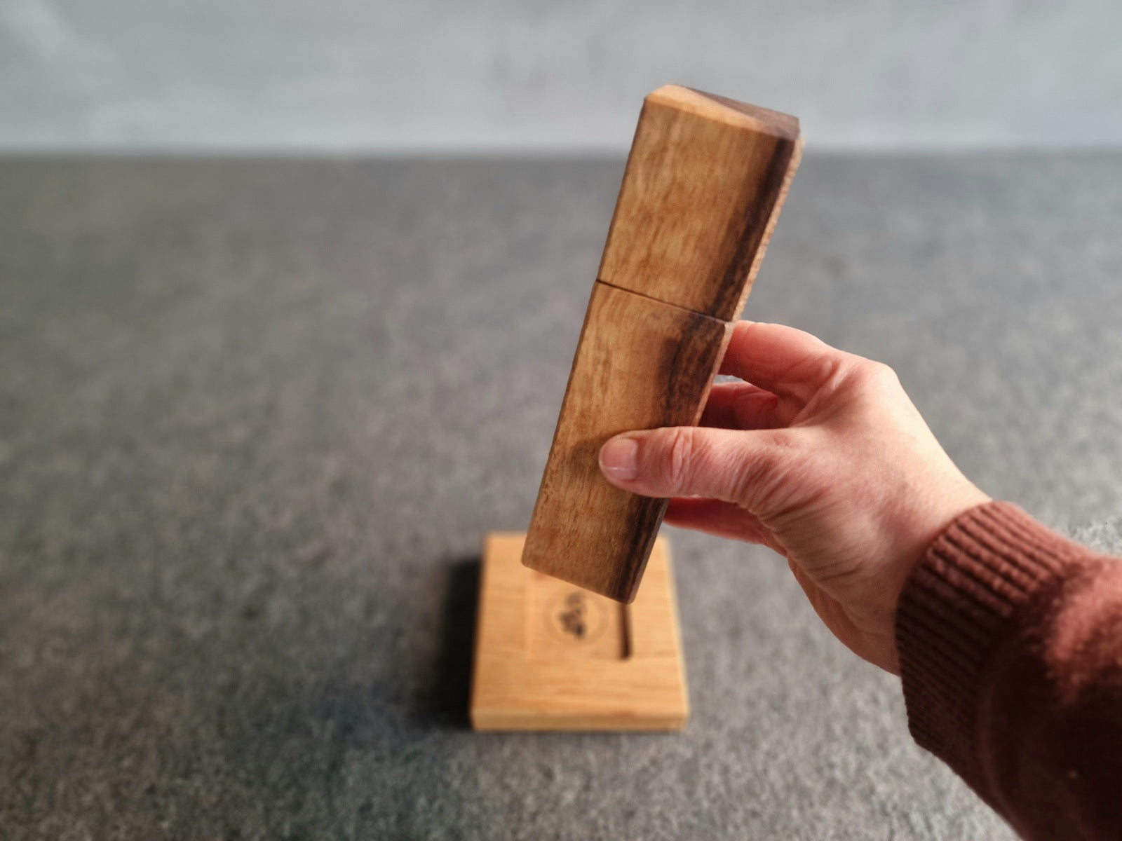 Hand hält eine Salzmühle aus Ovenkol mit Splint über einem Holzuntersetzer aus Eiche.