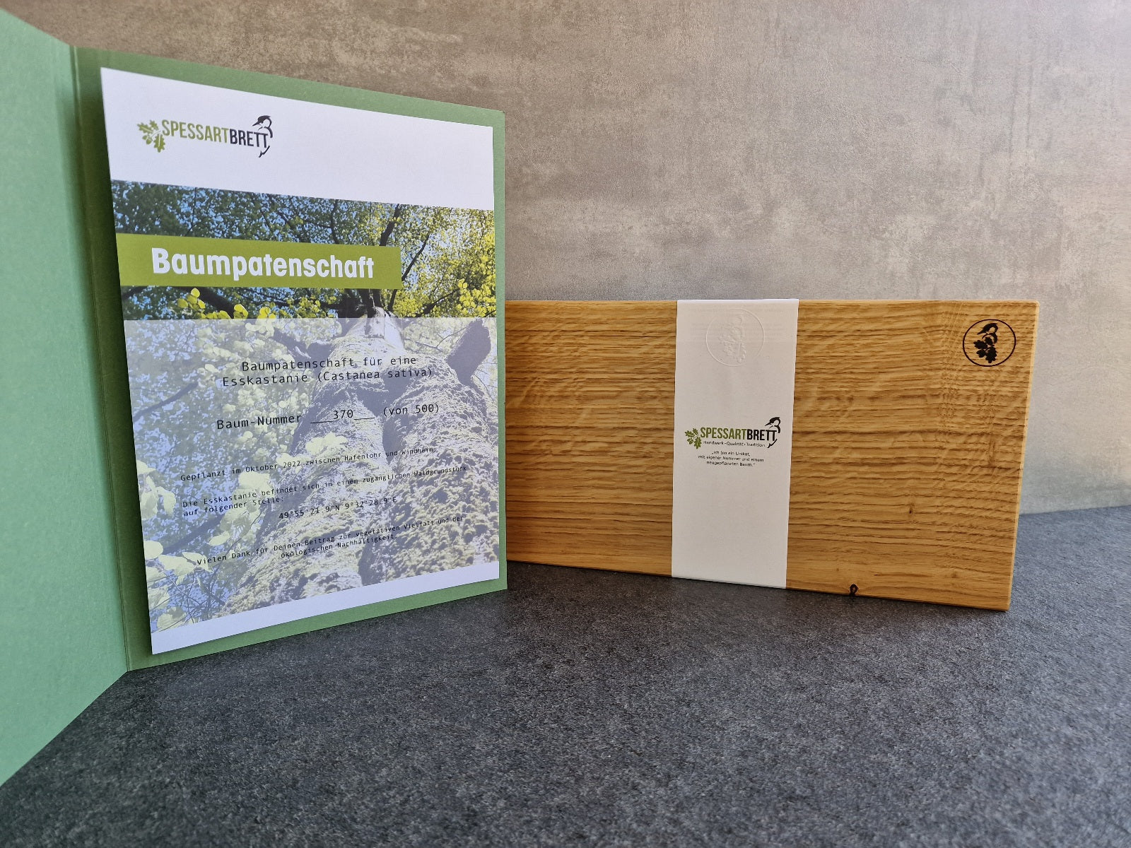 Mappe mit einer Baumpatenschafts-Urkunde und einem Eiche Gemüsebrett mit einer Spessartbrett-Banderole.