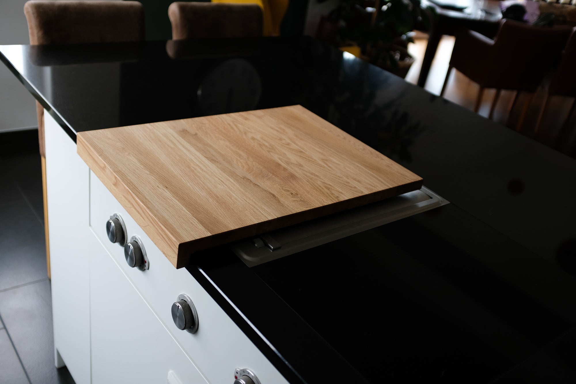 Design Küchensinsel mit Nero Assoluto Platte auf der ein Bora Kochfeld eingelassen ist. Auf dem Kochfeld liegt eine Eichenholz Abdeckung